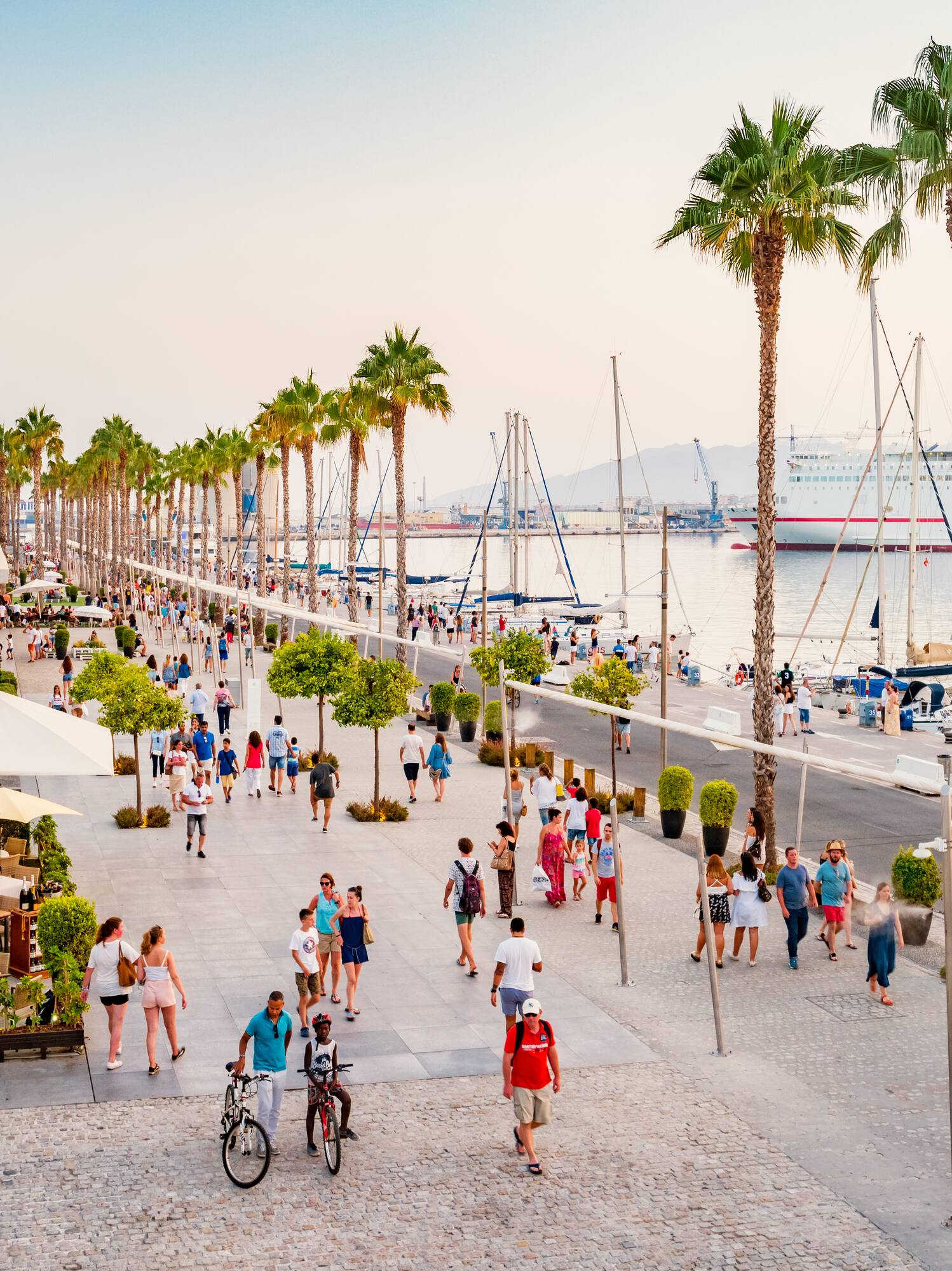 Muelle Uno Málaga: paseo con palmeras, gente, ferry y barcos en puerto.