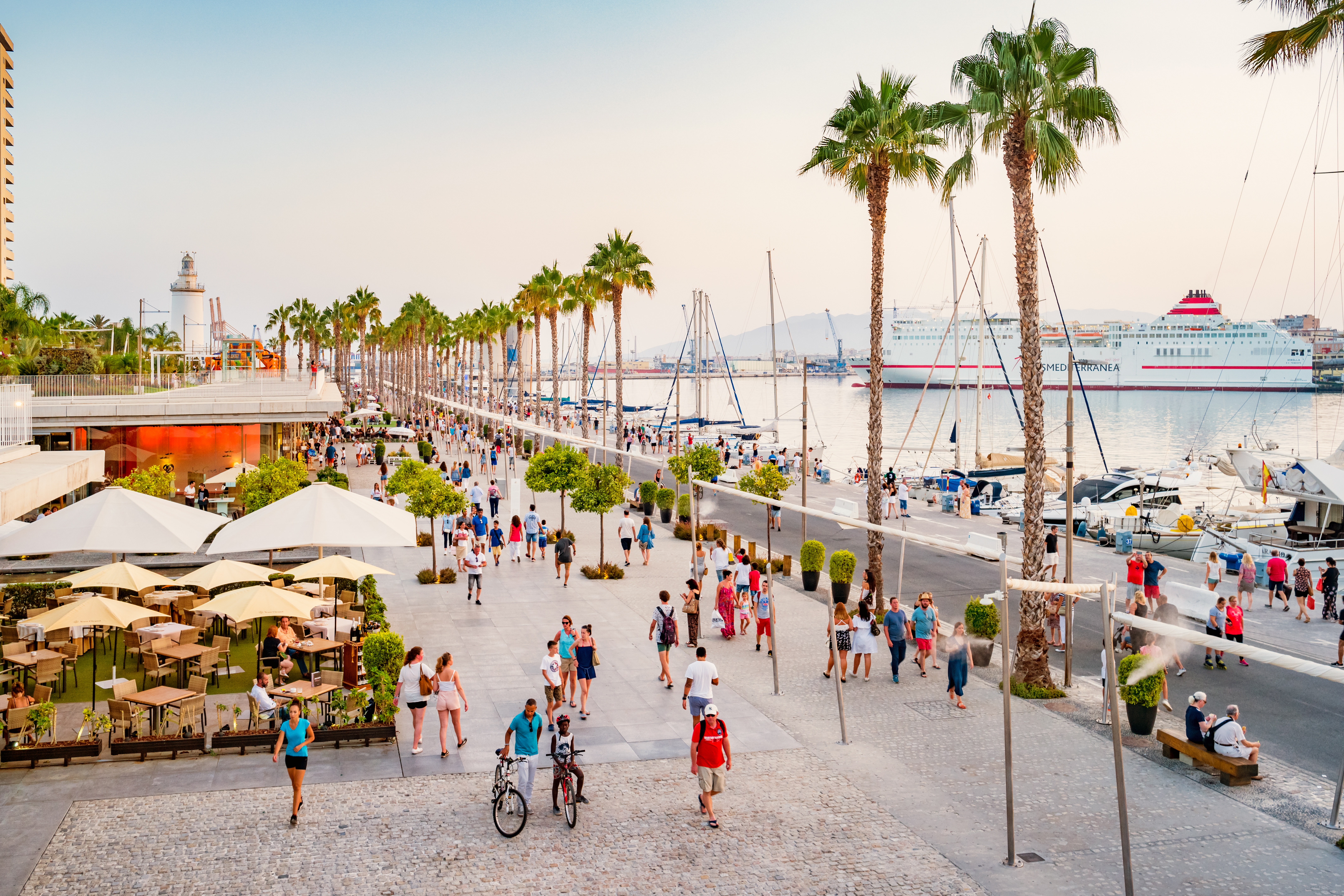 Muelle Uno Málaga: paseo con palmeras, gente, ferry y barcos en puerto.