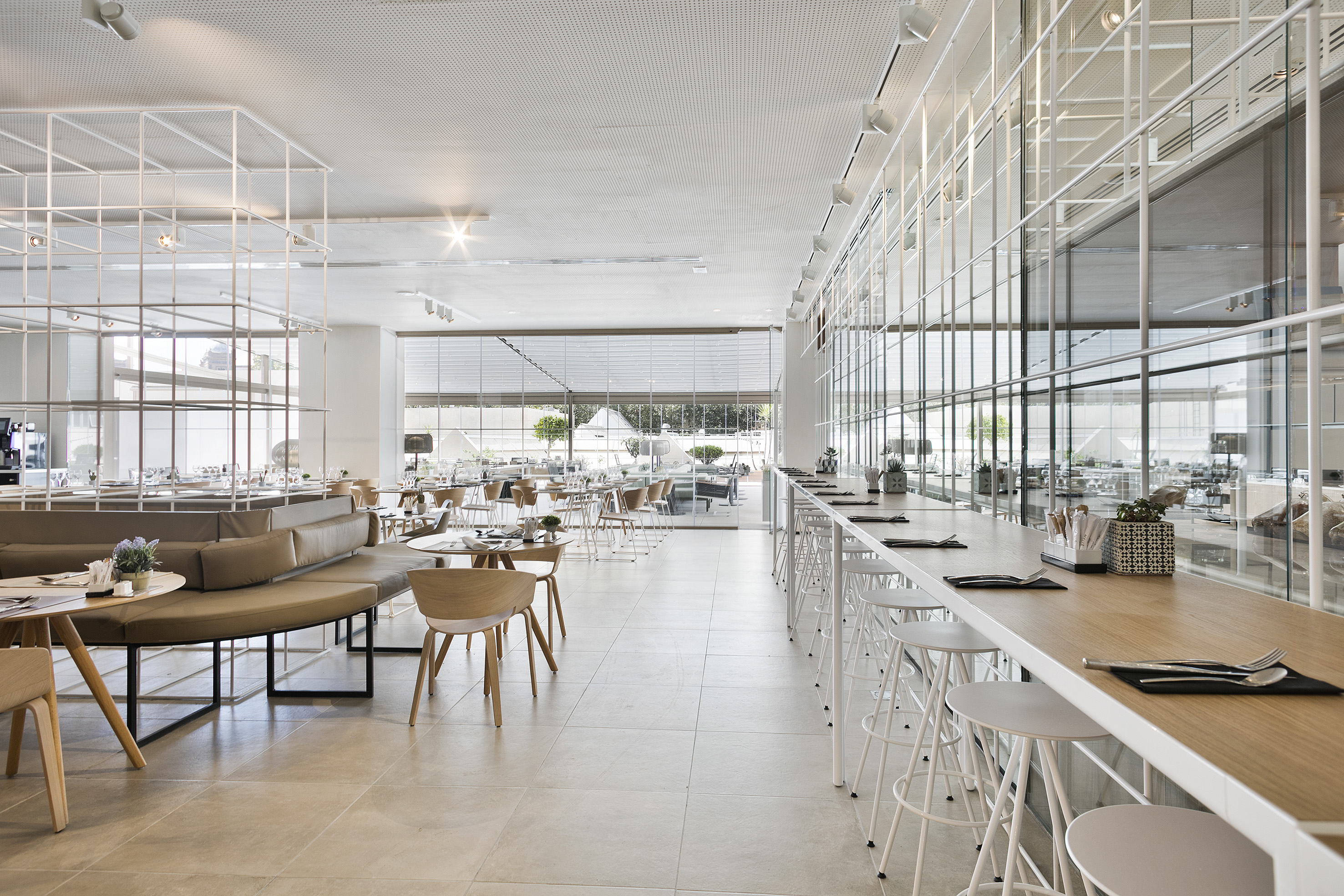 Bright modern restaurant interior with long bar, white stools, and booth seating.