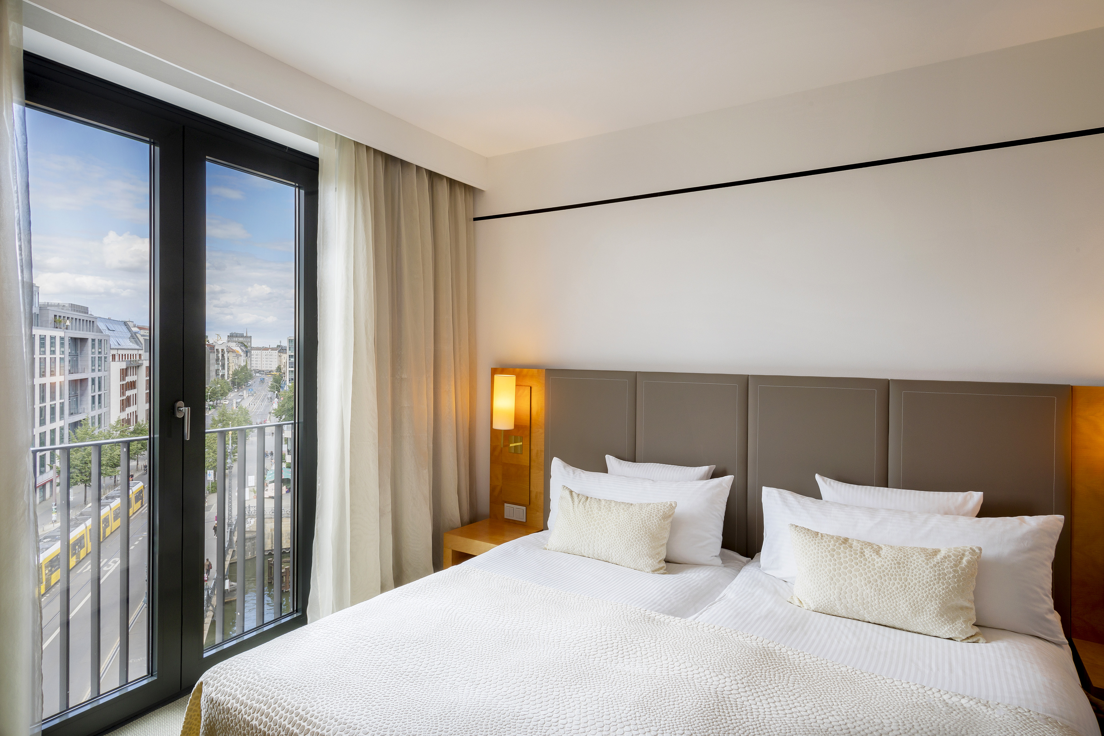 Modern hotel room with comfortable bed, city view, and tram on street.