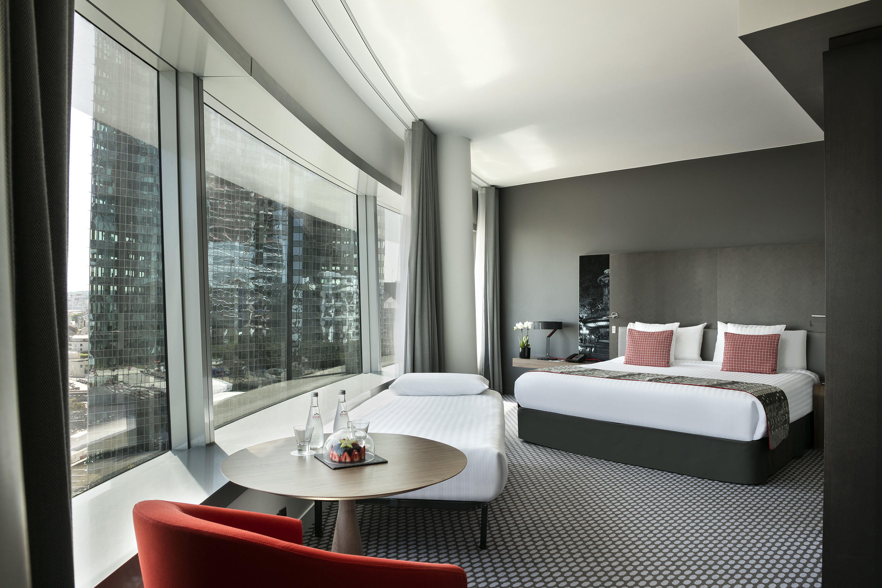 Modern hotel room with king bed, single bed, city view, and contemporary style.
