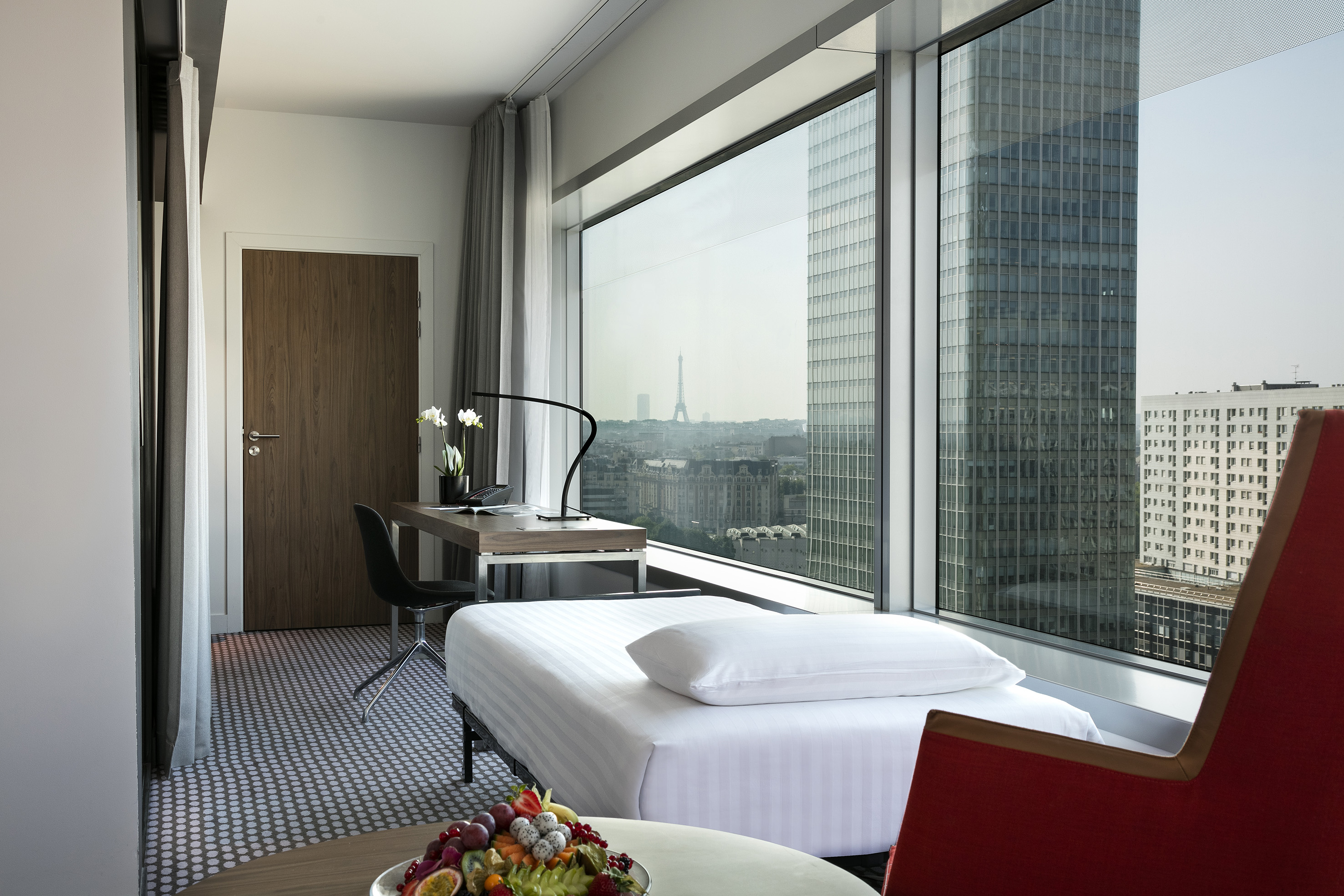 Paris hotel room with Eiffel Tower view, modern desk, bed, and city skyline.