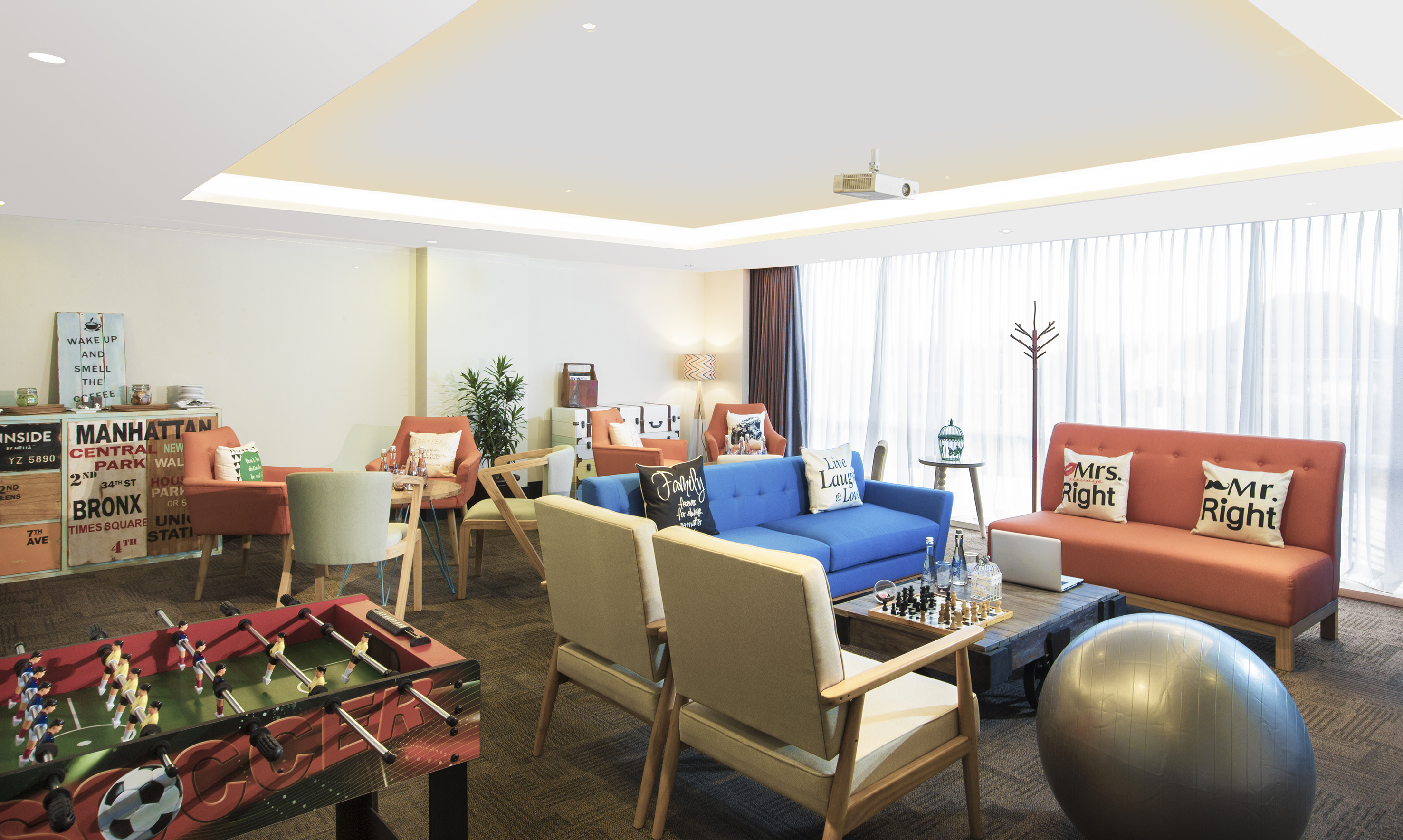 Modern common area lounge with foosball, blue sofa, orange seating, and chess.