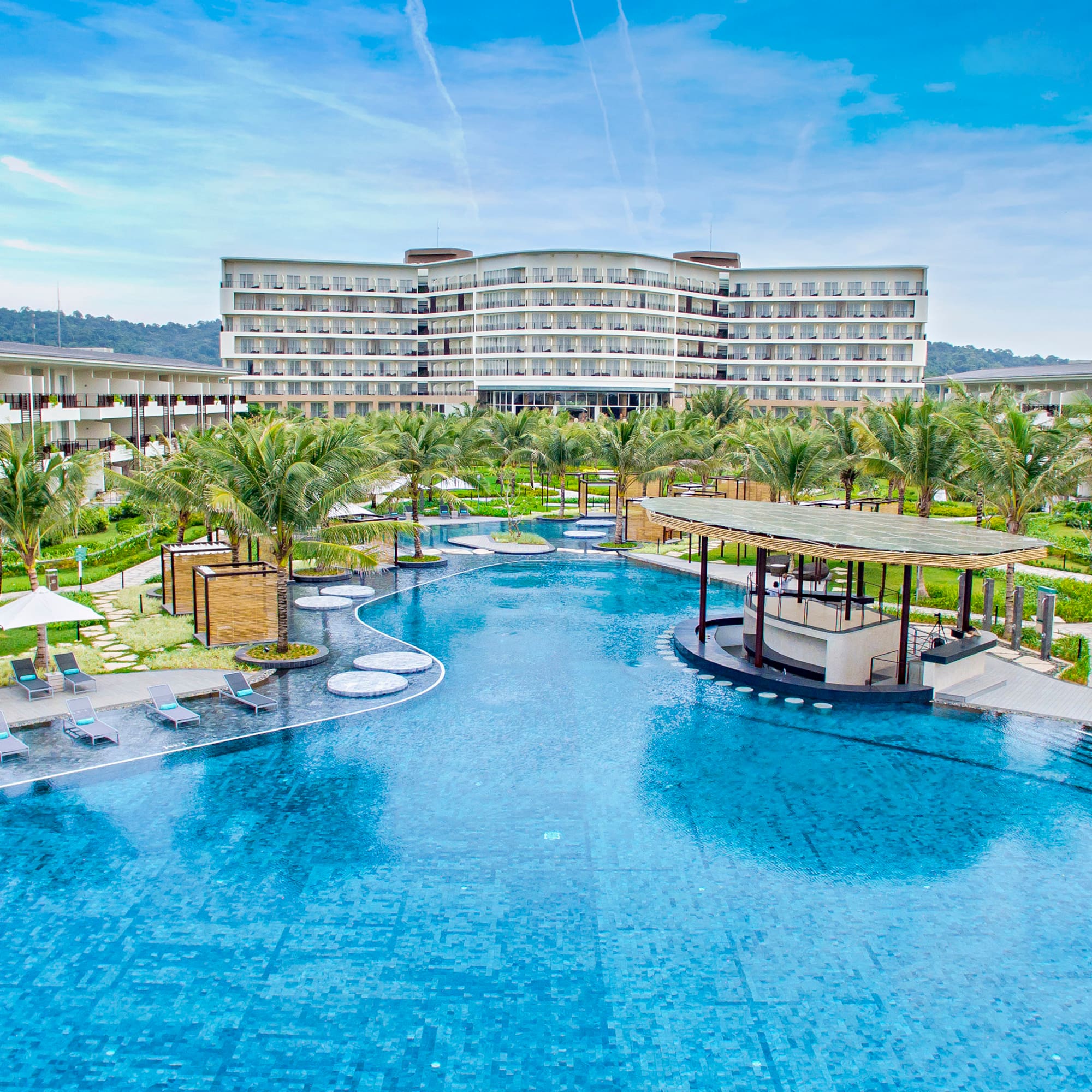 Expansive resort hotel with large outdoor swimming pool, palm trees, and a pool bar.