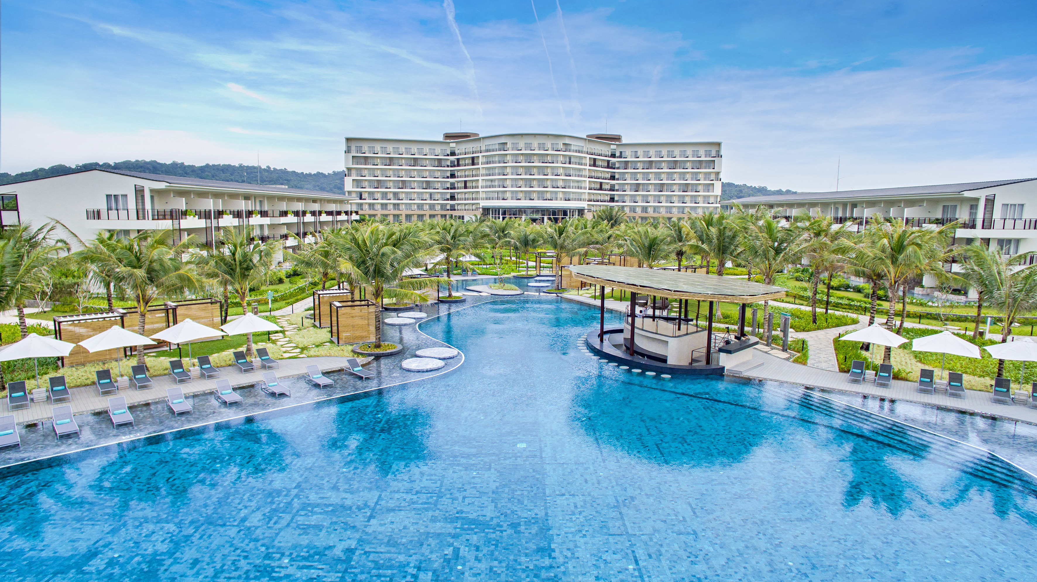 Luxury resort pool with palm trees and hotel complex.