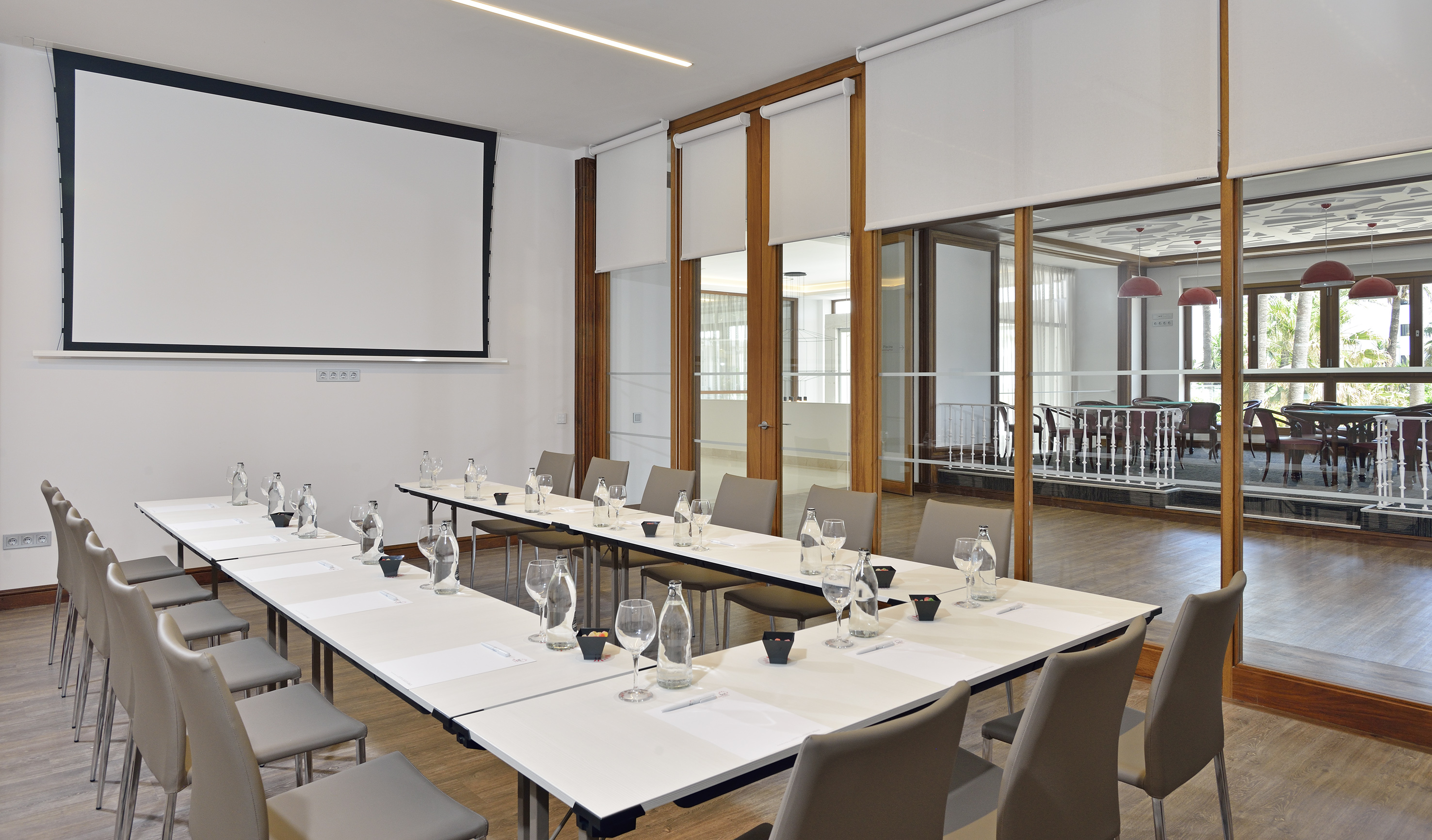 Modern conference room with U-shaped table, projector screen, and glass partitions.