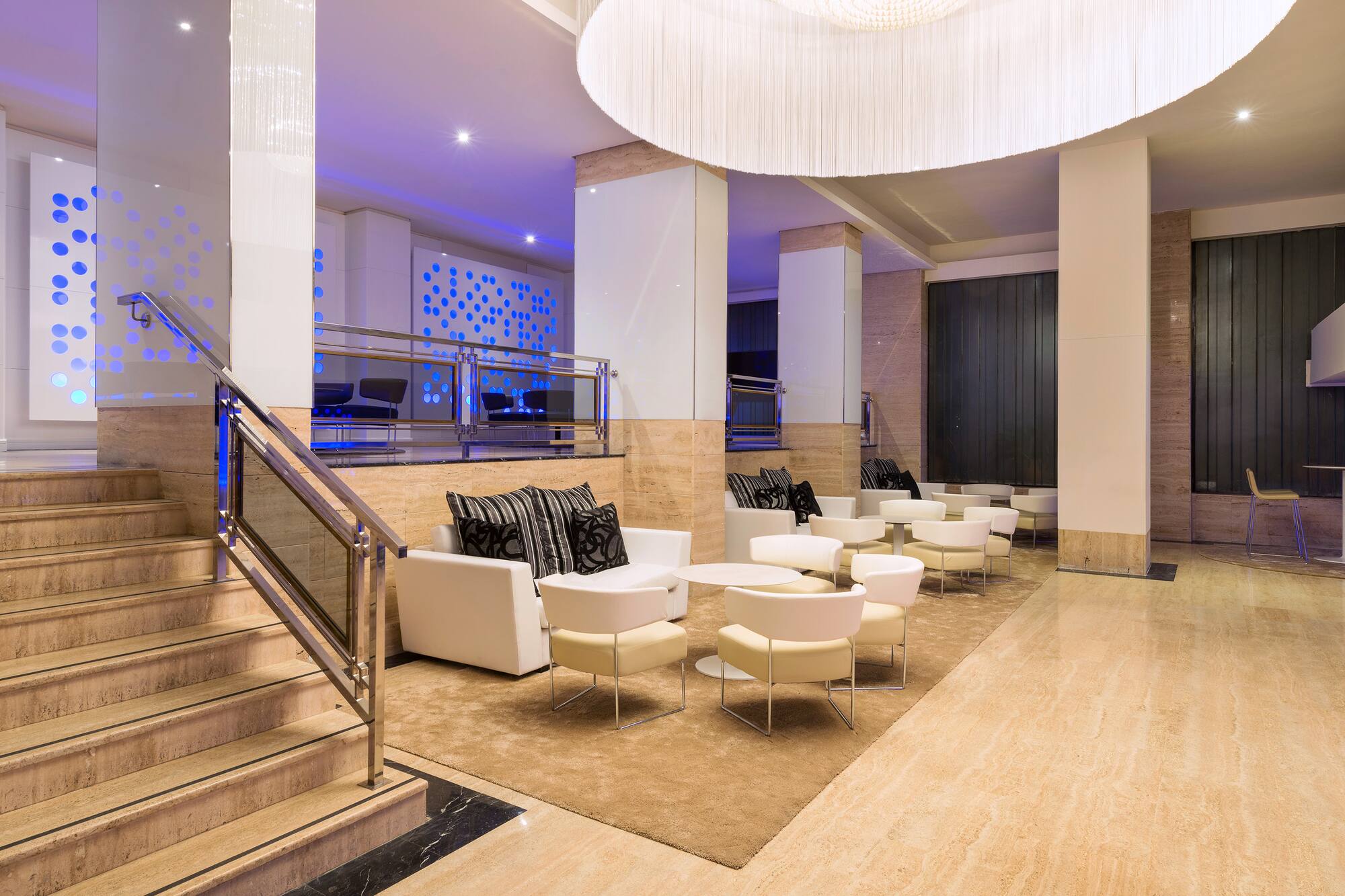 Modern hotel lobby lounge with white seating, marble stairs, and blue lighting.