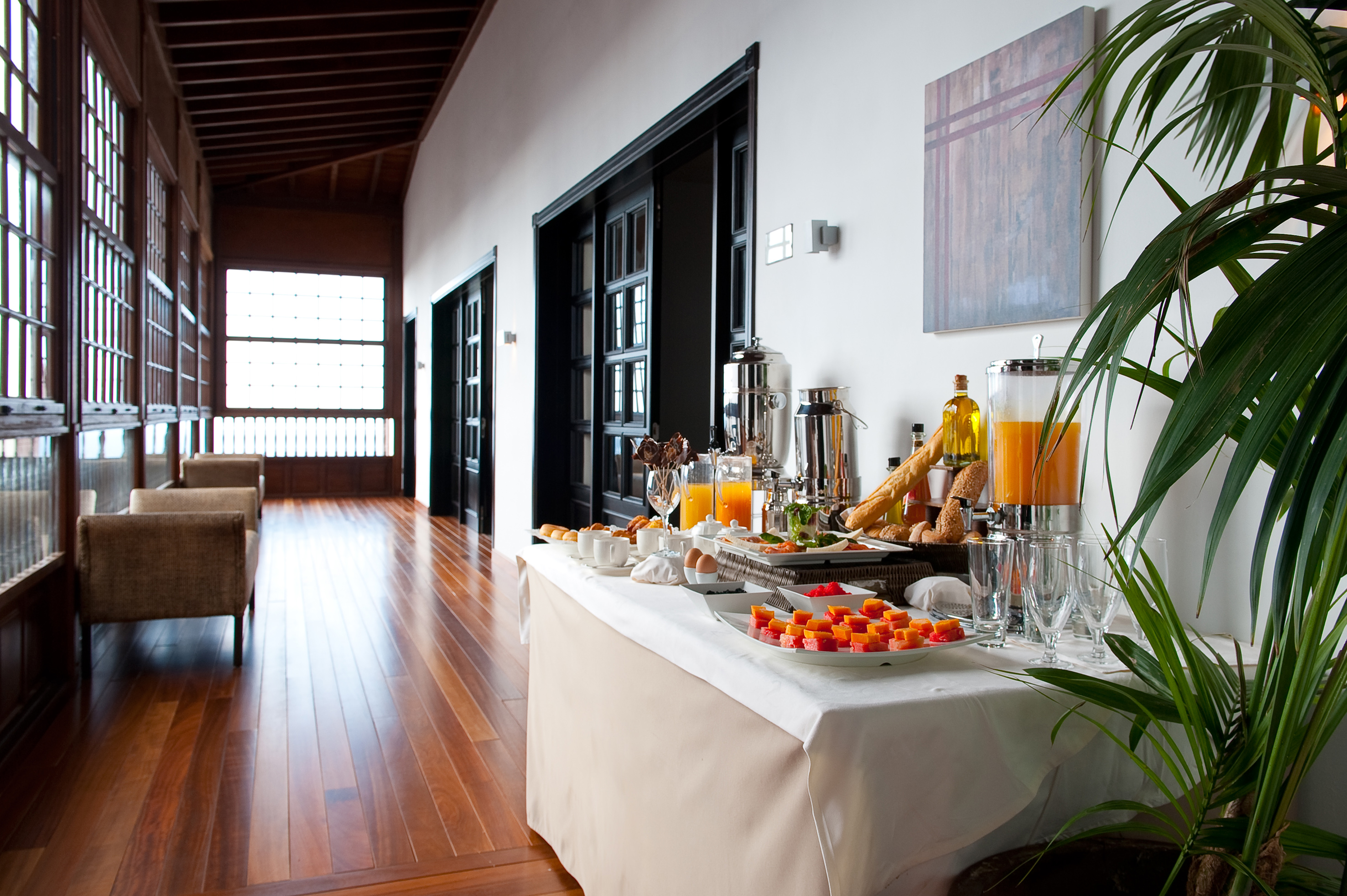 Hotel breakfast buffet in a corridor with wooden floors and seating.