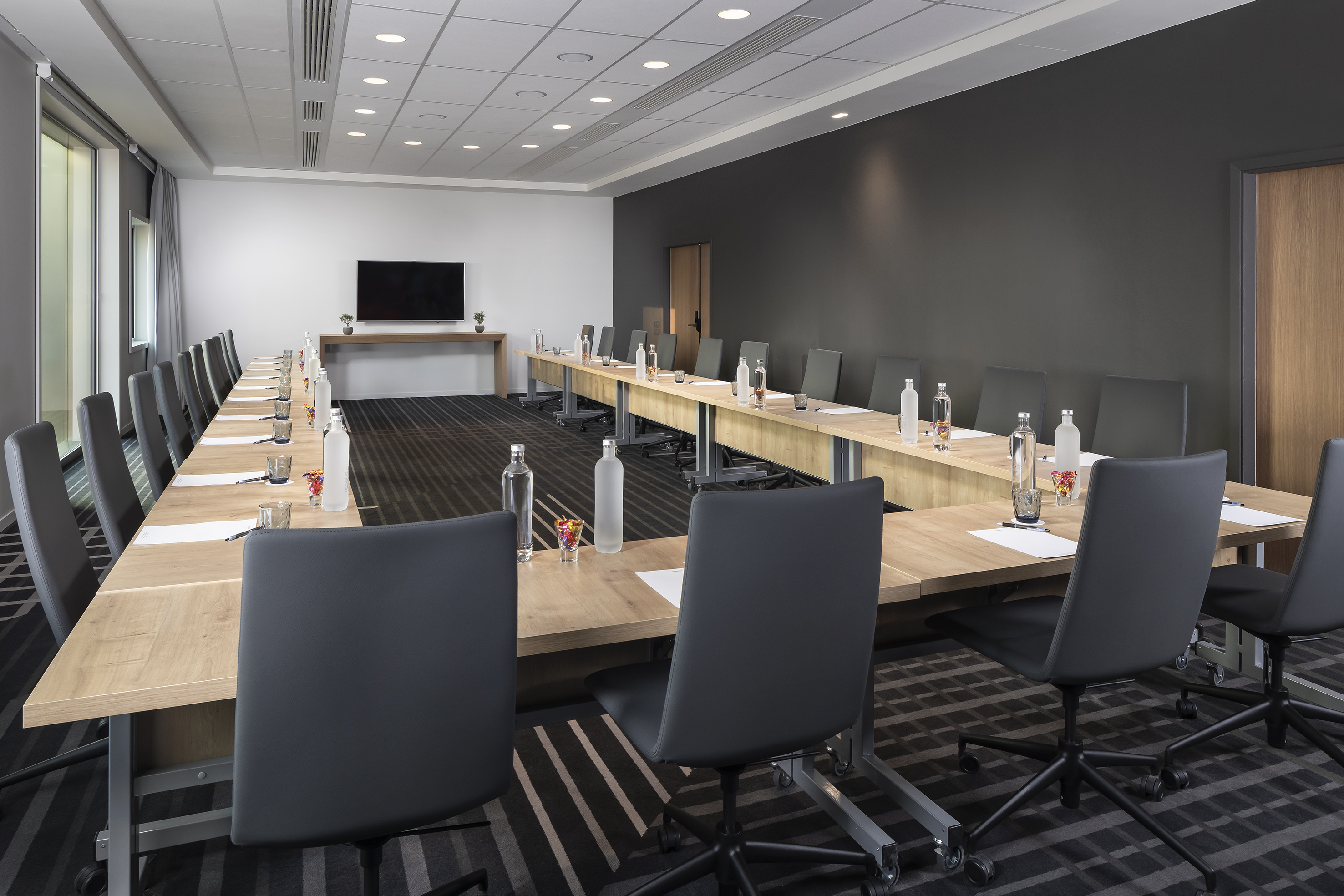 Modern conference room with U-shaped table, black chairs, and presentation screen.