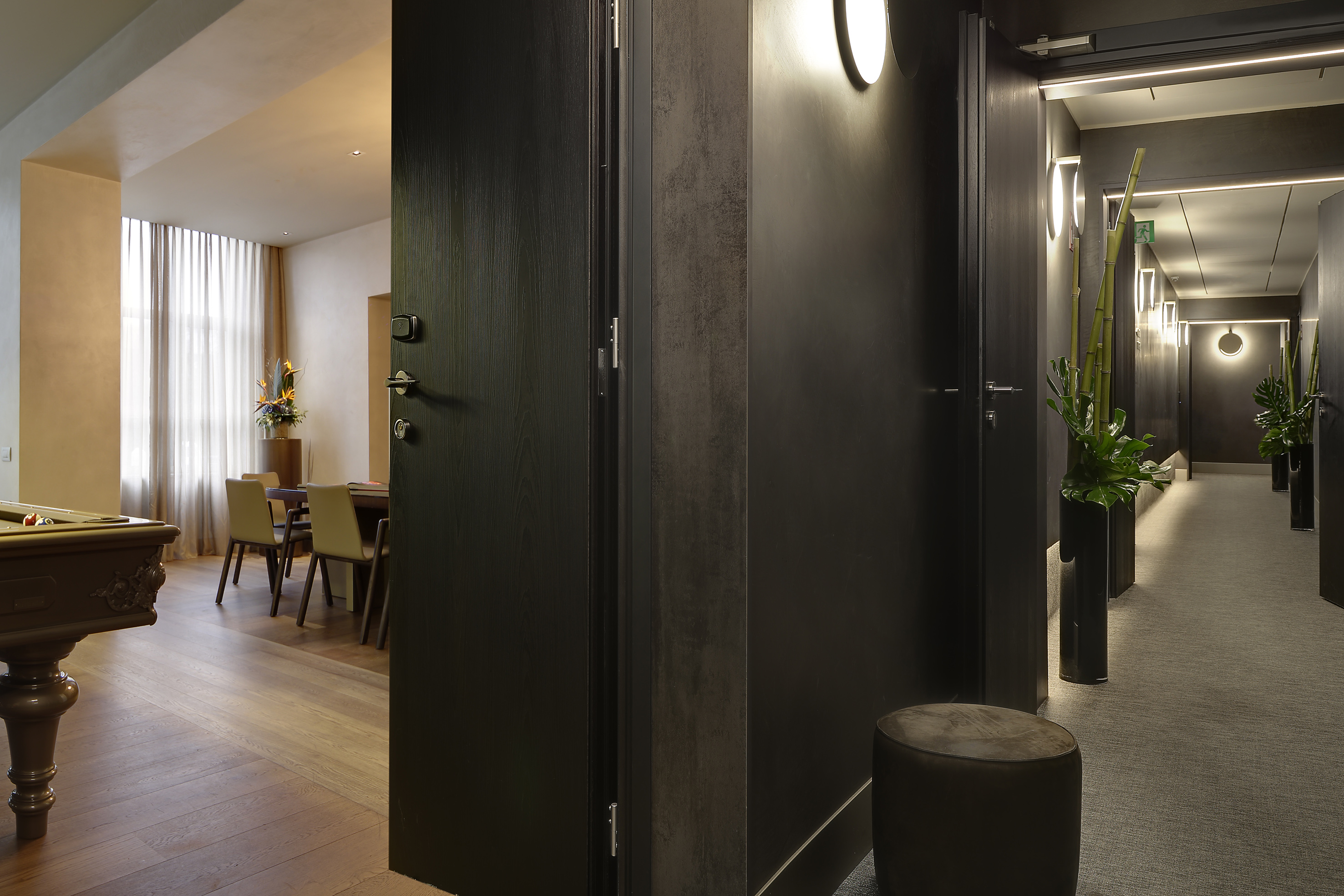 Dark, modern hallway with doors; bright room with pool table, dining area.