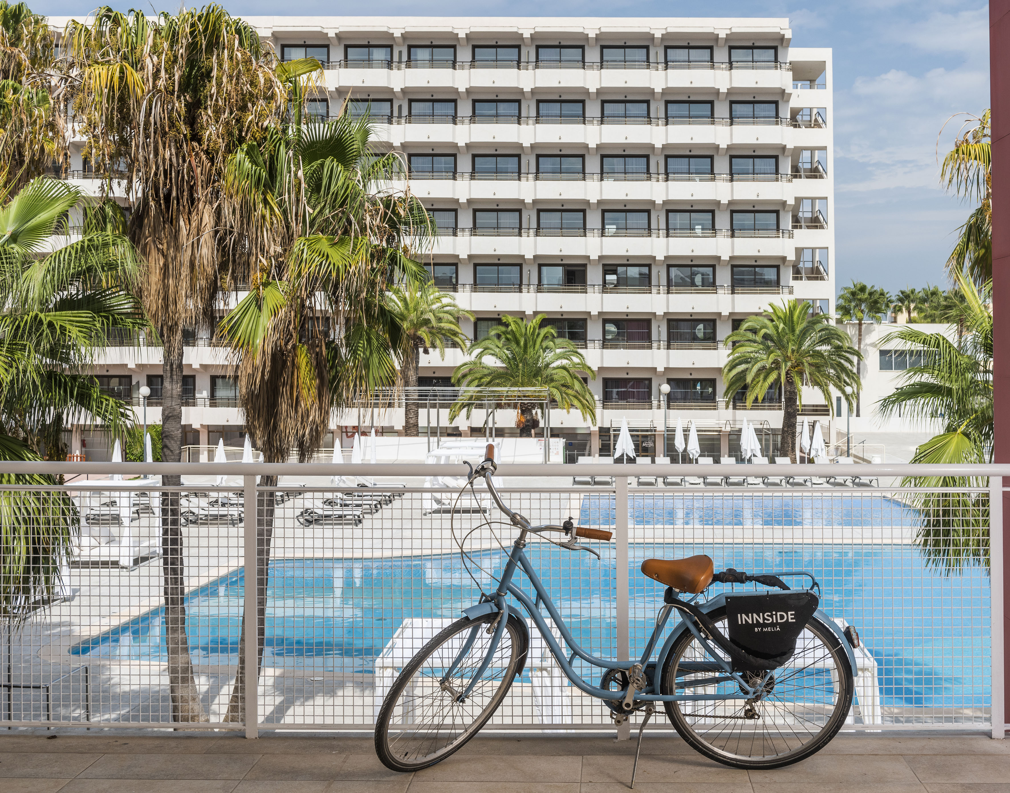 Blue bicycle overlooking hotel pool, palm trees, and Innside by Meliá resort.