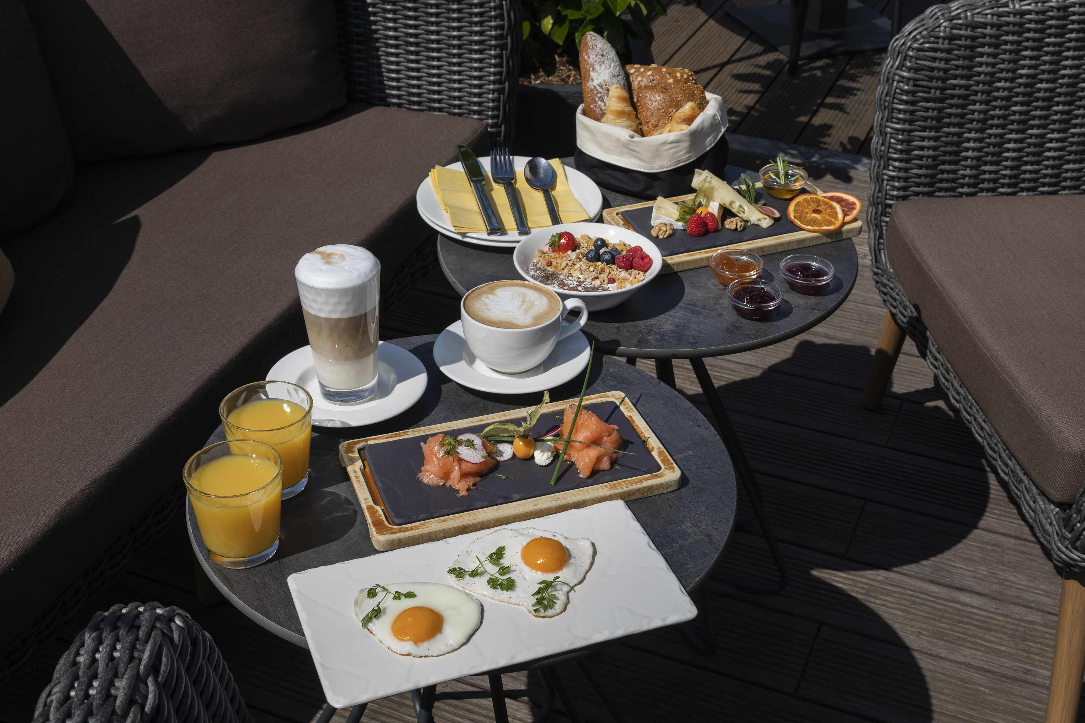 Sunny outdoor breakfast: coffee, eggs, smoked salmon, granola, bread, cheese, juice.