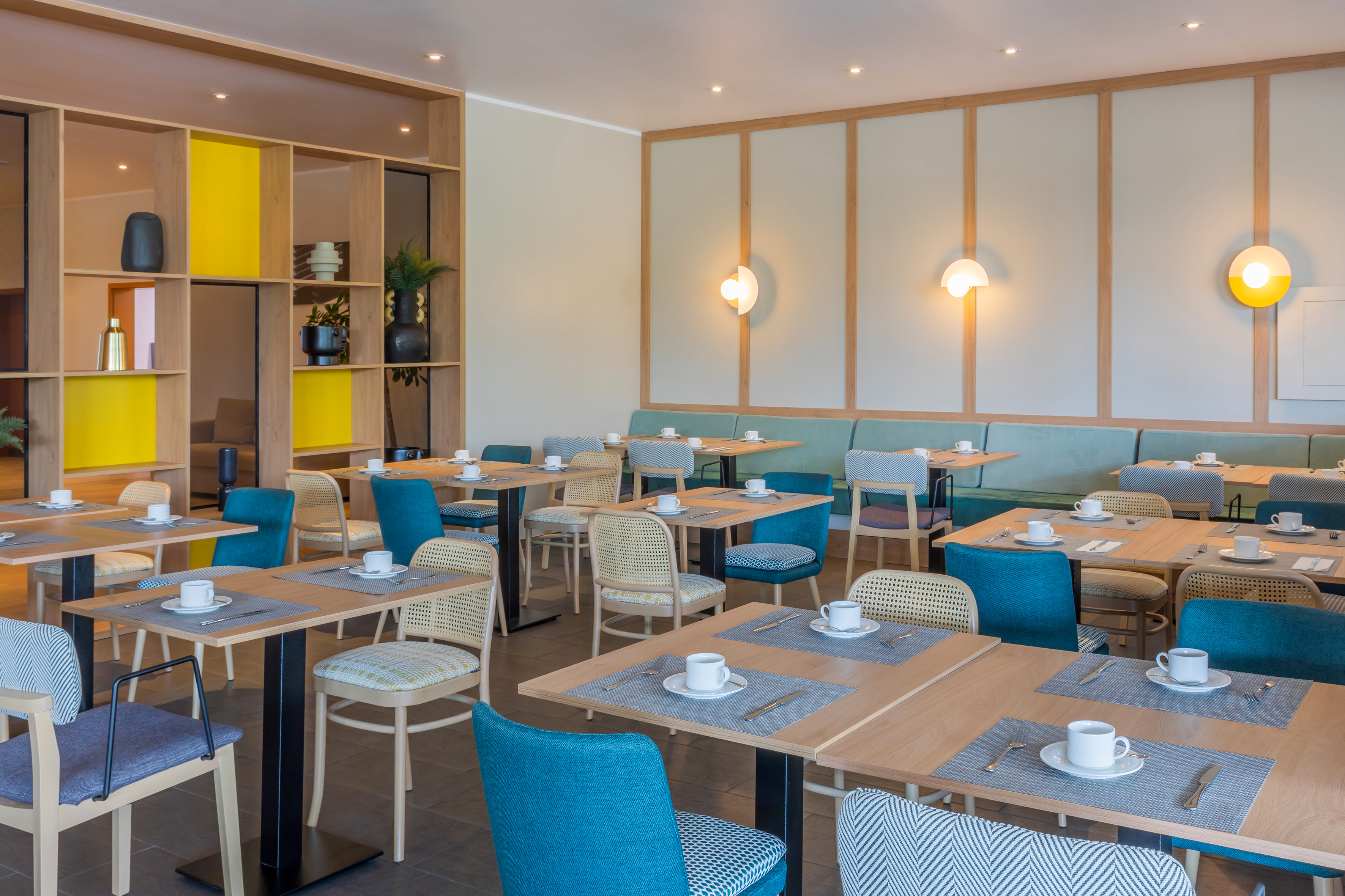 Modern hotel dining room with breakfast tables, colorful seating, green banquette, and stylish decor.
