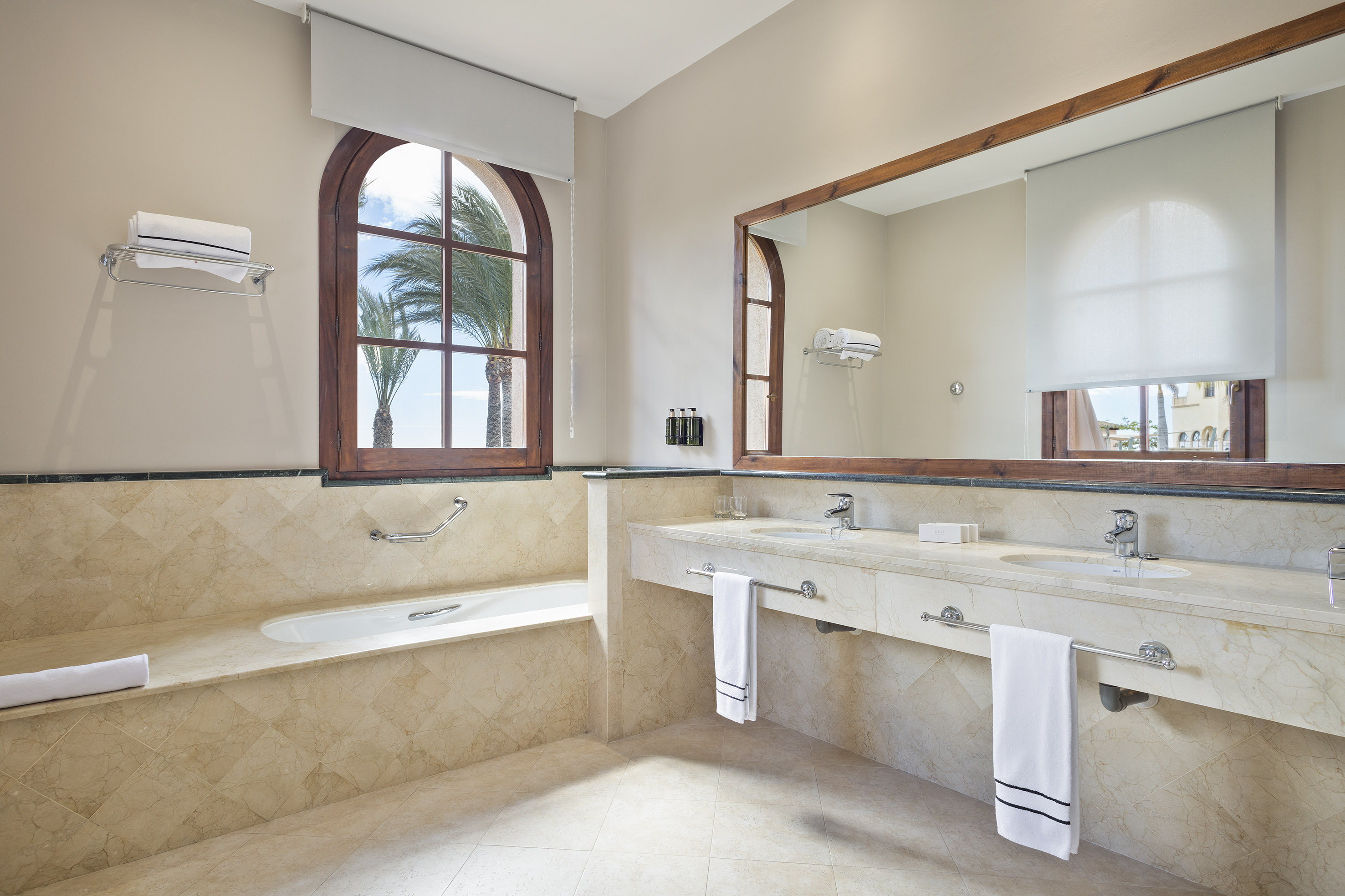 Luxury marble bathroom with double vanity, bathtub, and tropical window.