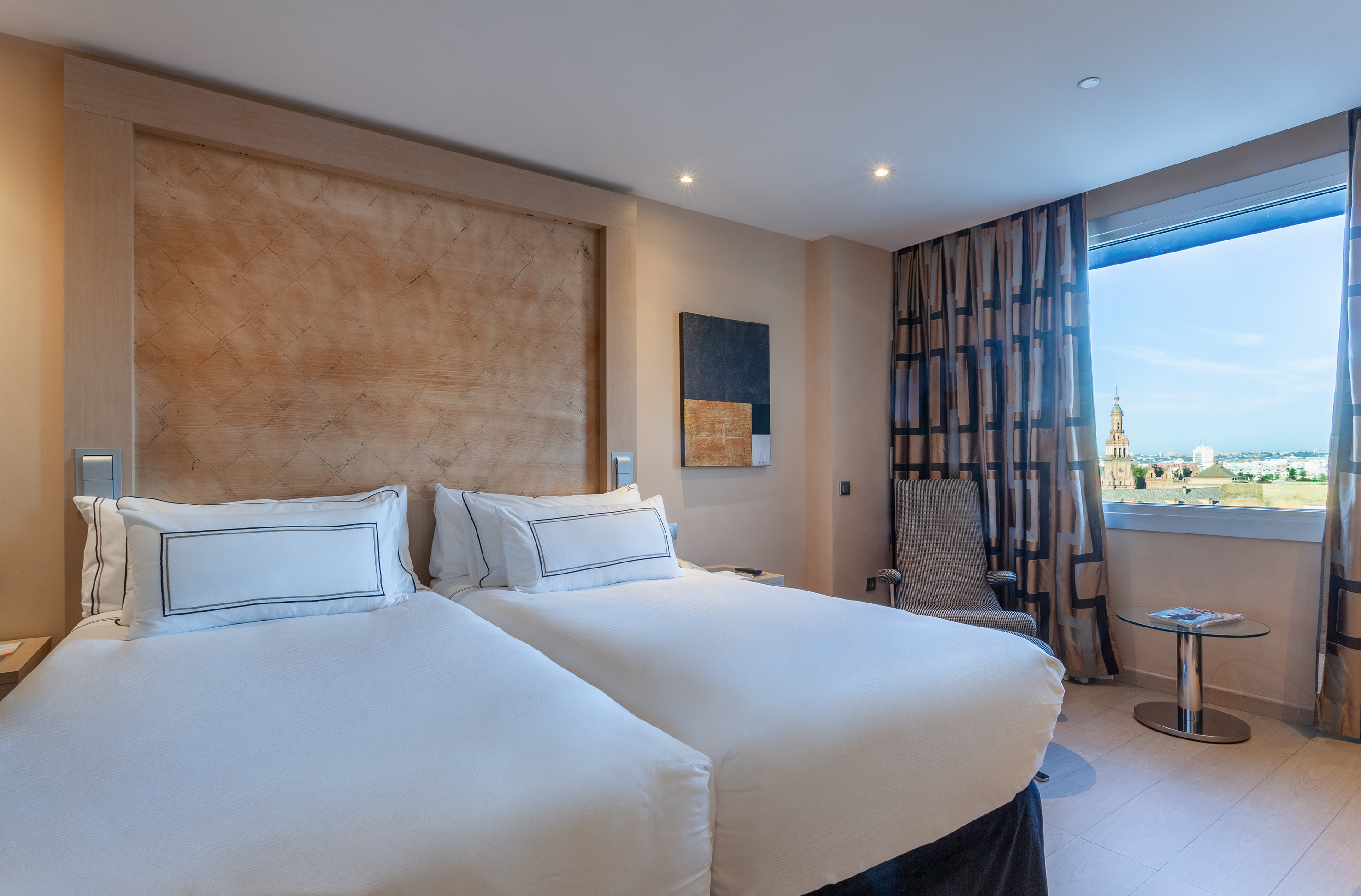 Modern hotel room with twin beds, wooden headboard, and city view window.