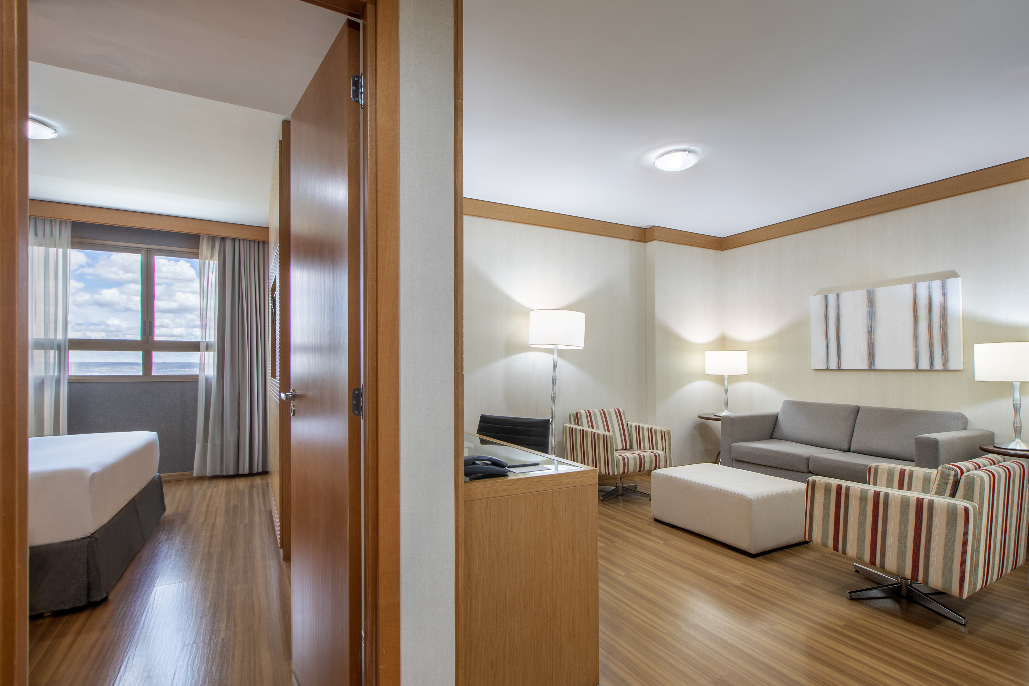 Hotel suite: living room with sofa, striped chairs, wood floor, and bedroom.
