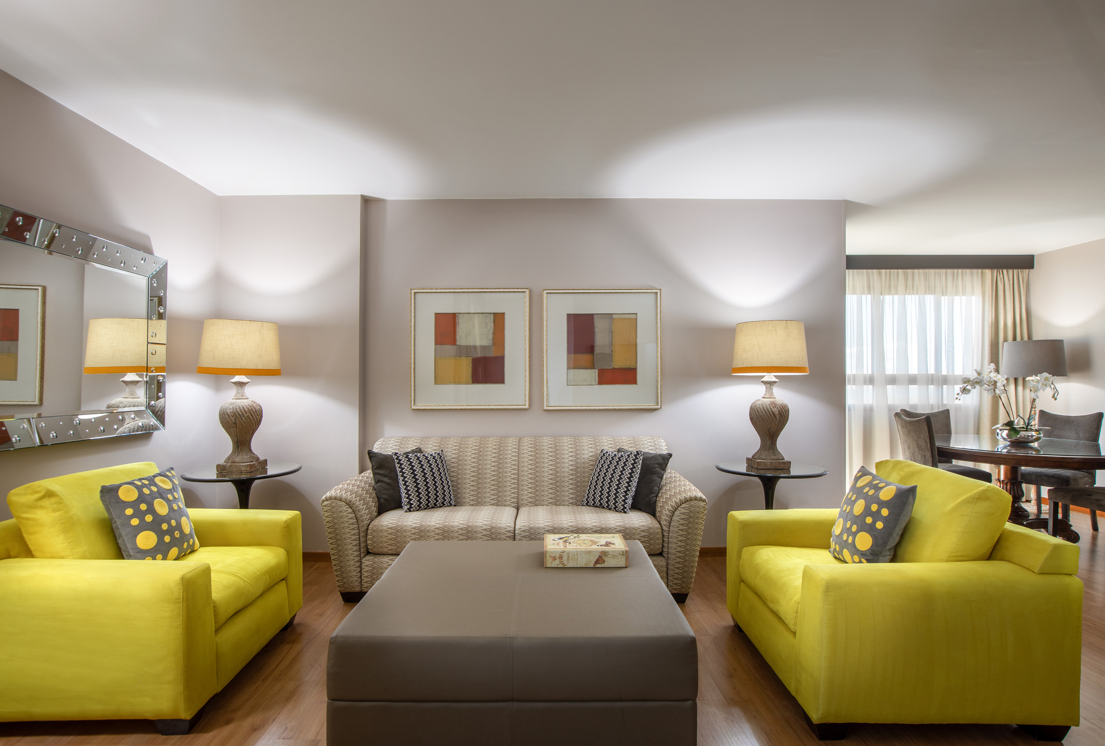 Vibrant living room with yellow armchairs, patterned sofa, and central ottoman.