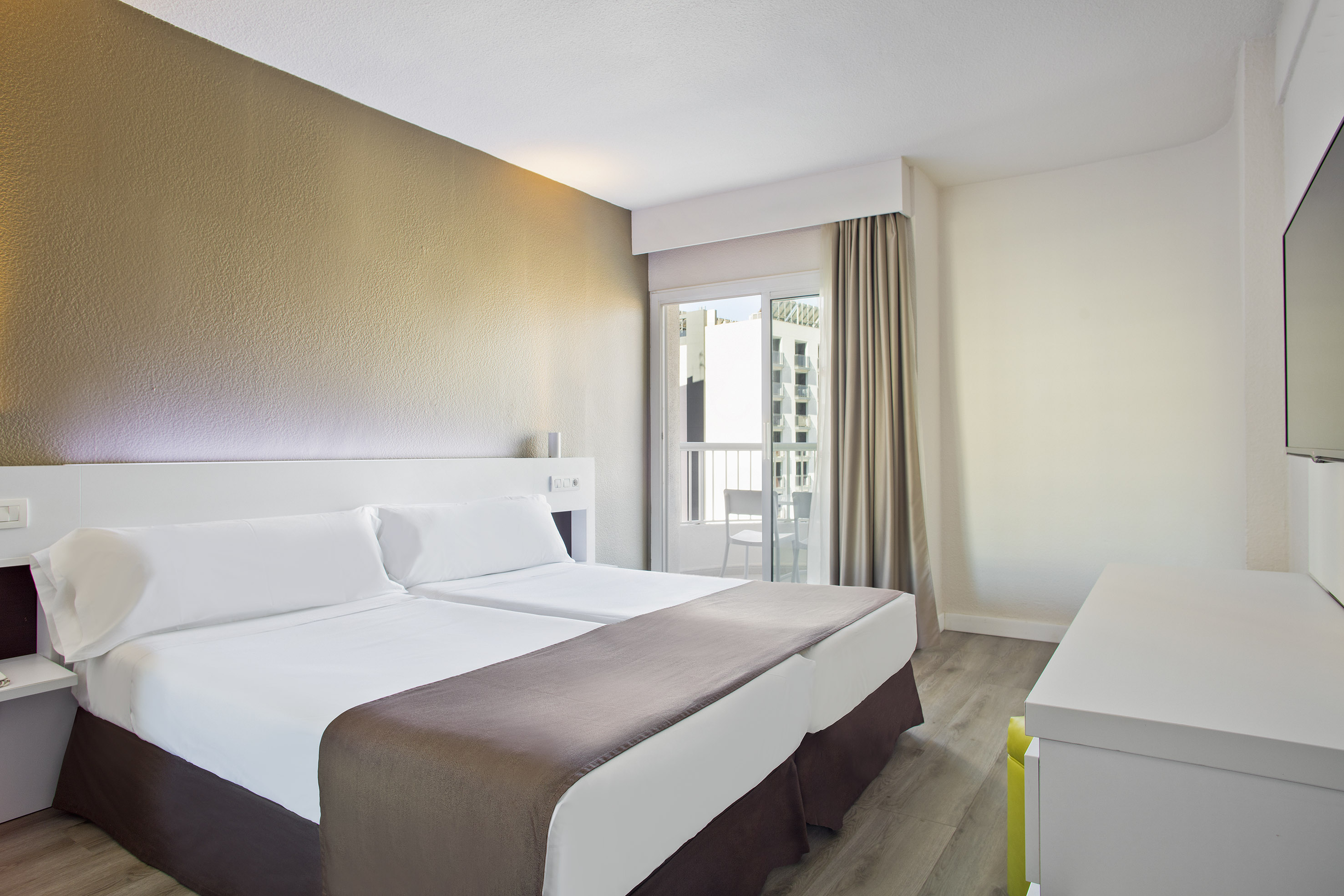 Bright hotel room with twin beds, textured wall, balcony, modern decor.