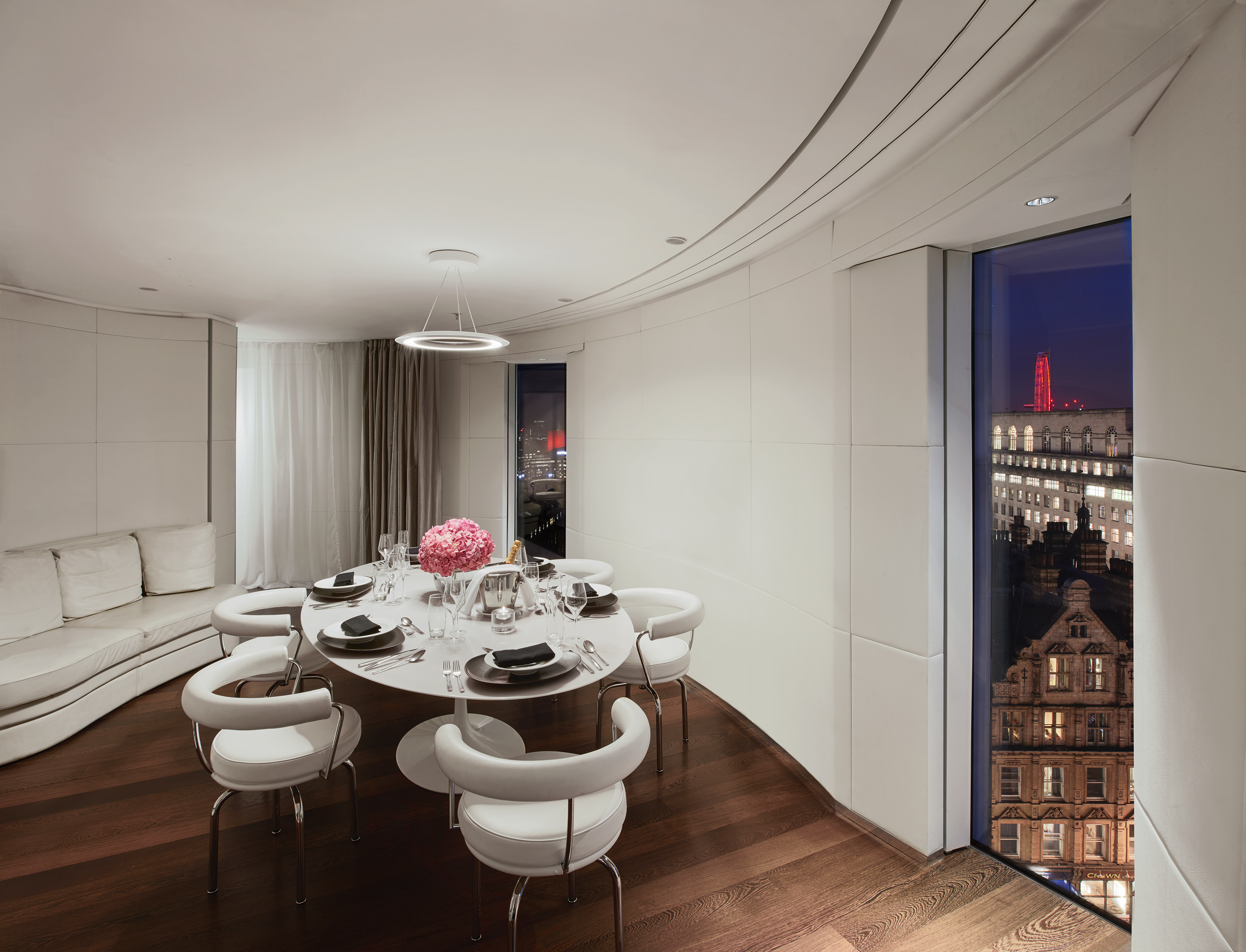 Sleek modern dining room with white table, flowers, and city night view.