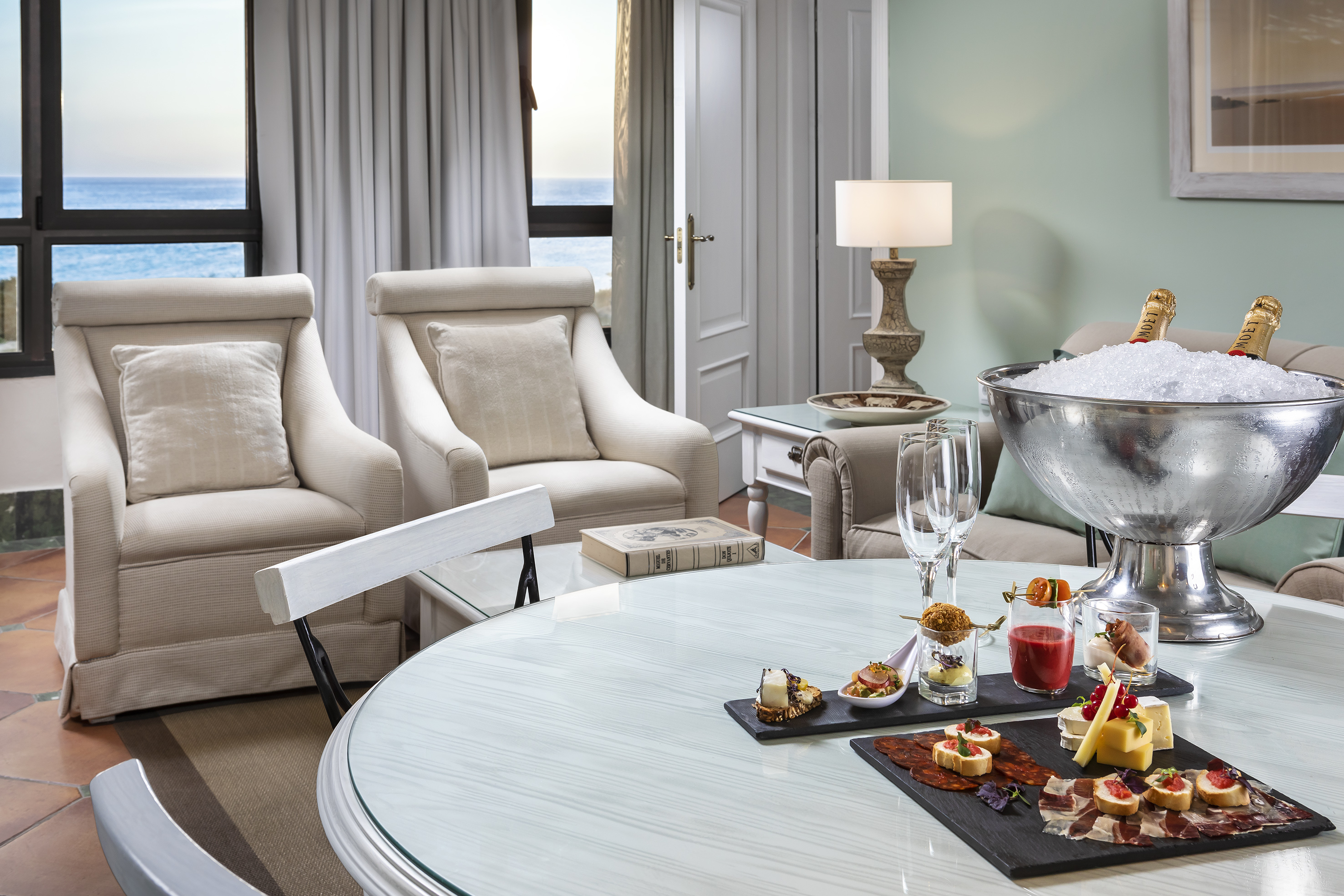 Luxury hotel ocean view suite with champagne, gourmet appetizers, and armchairs.