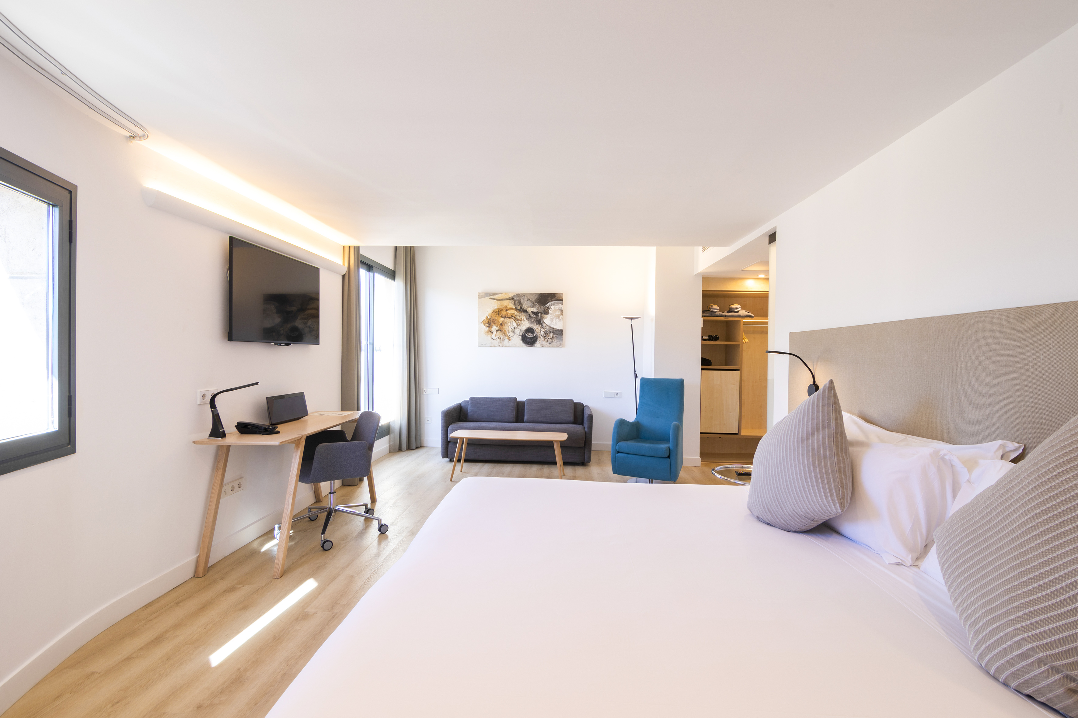 Bright, modern hotel suite with king bed, living area, desk, and TV.
