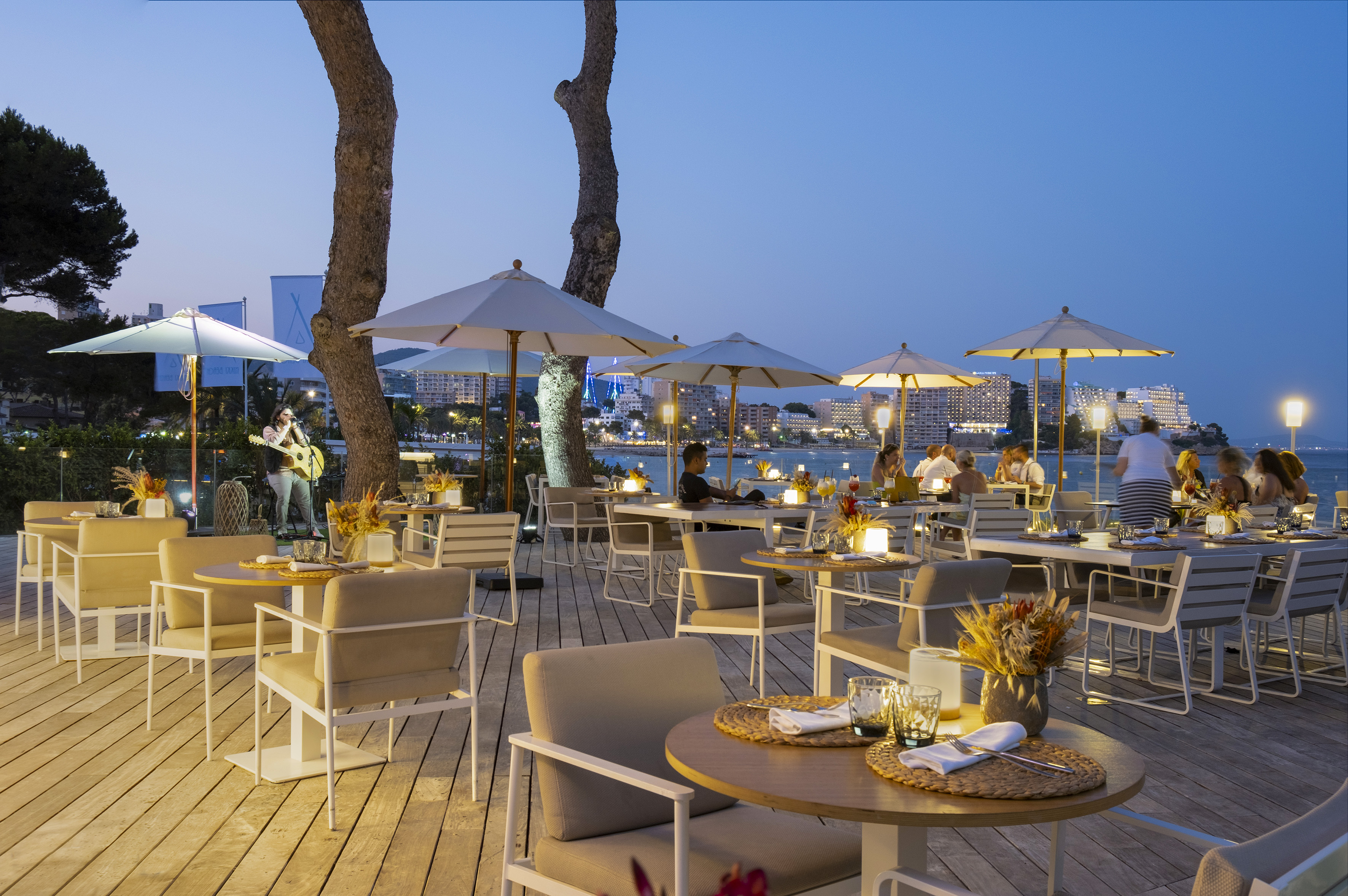 Waterfront outdoor dining at dusk with live music and ambient lighting.