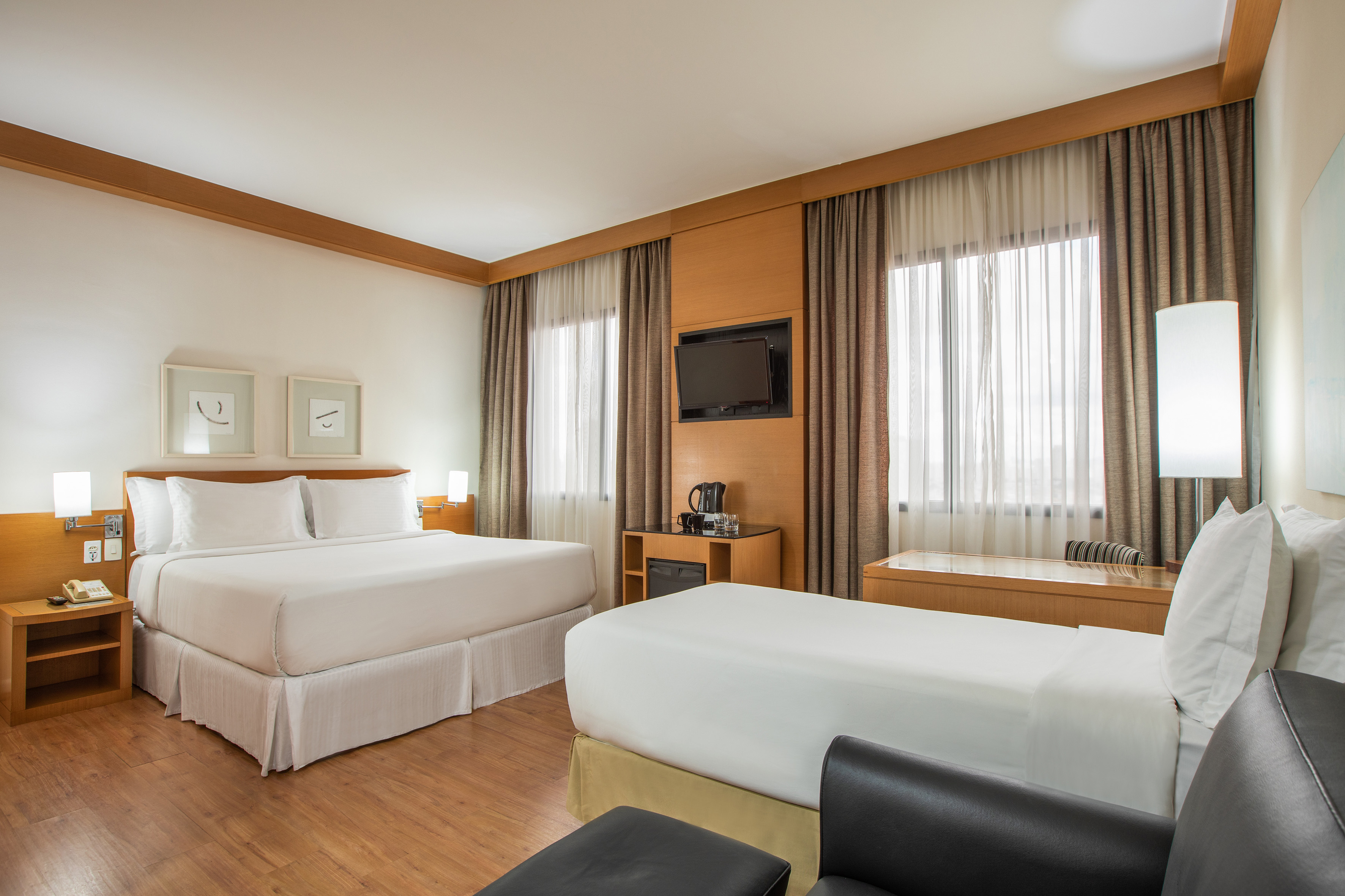 Hotel room with queen bed, single bed, modern decor, wood floor, and TV.
