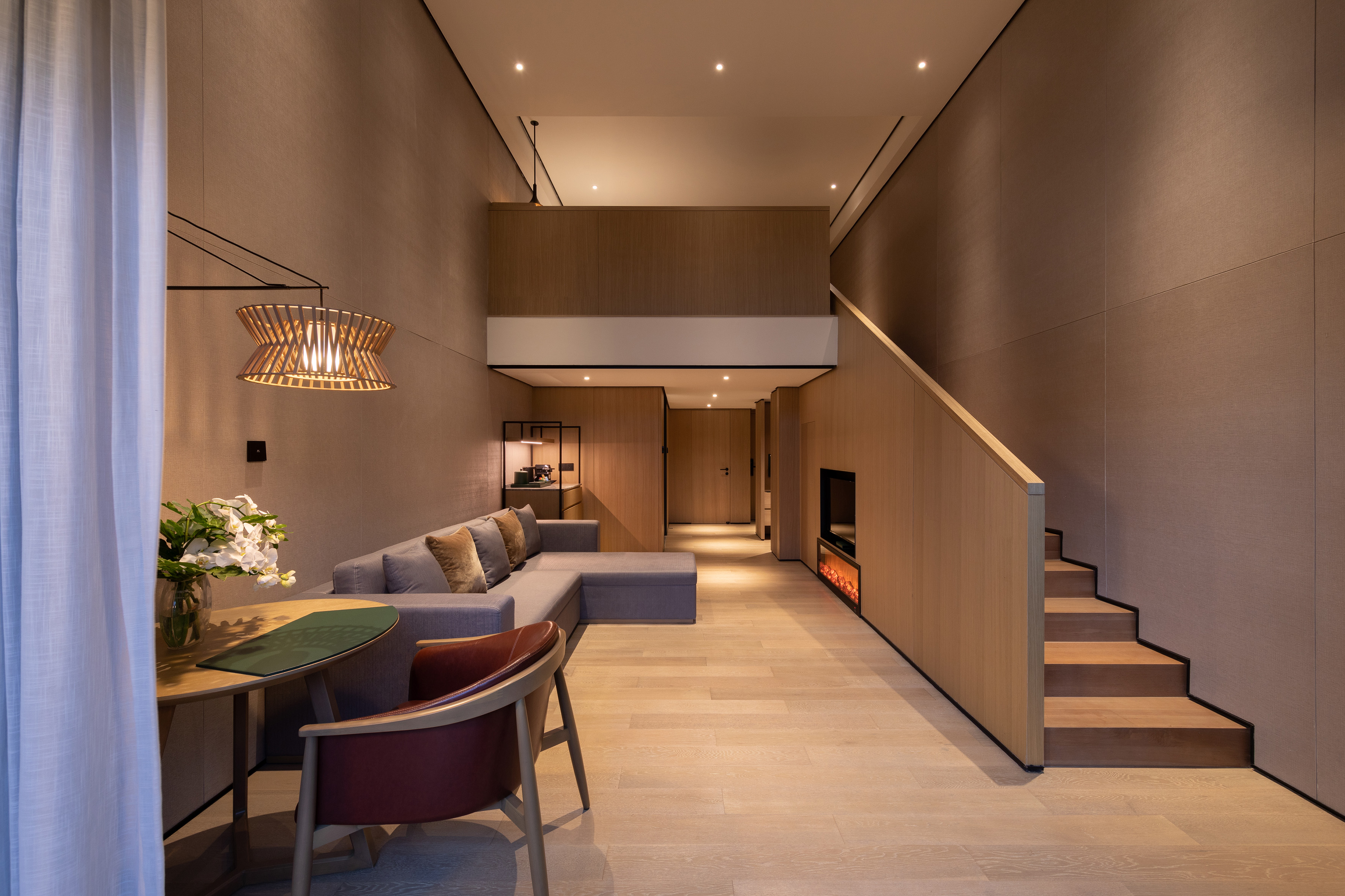 Modern loft living room with sectional sofa, wood staircase, and cozy fireplace.