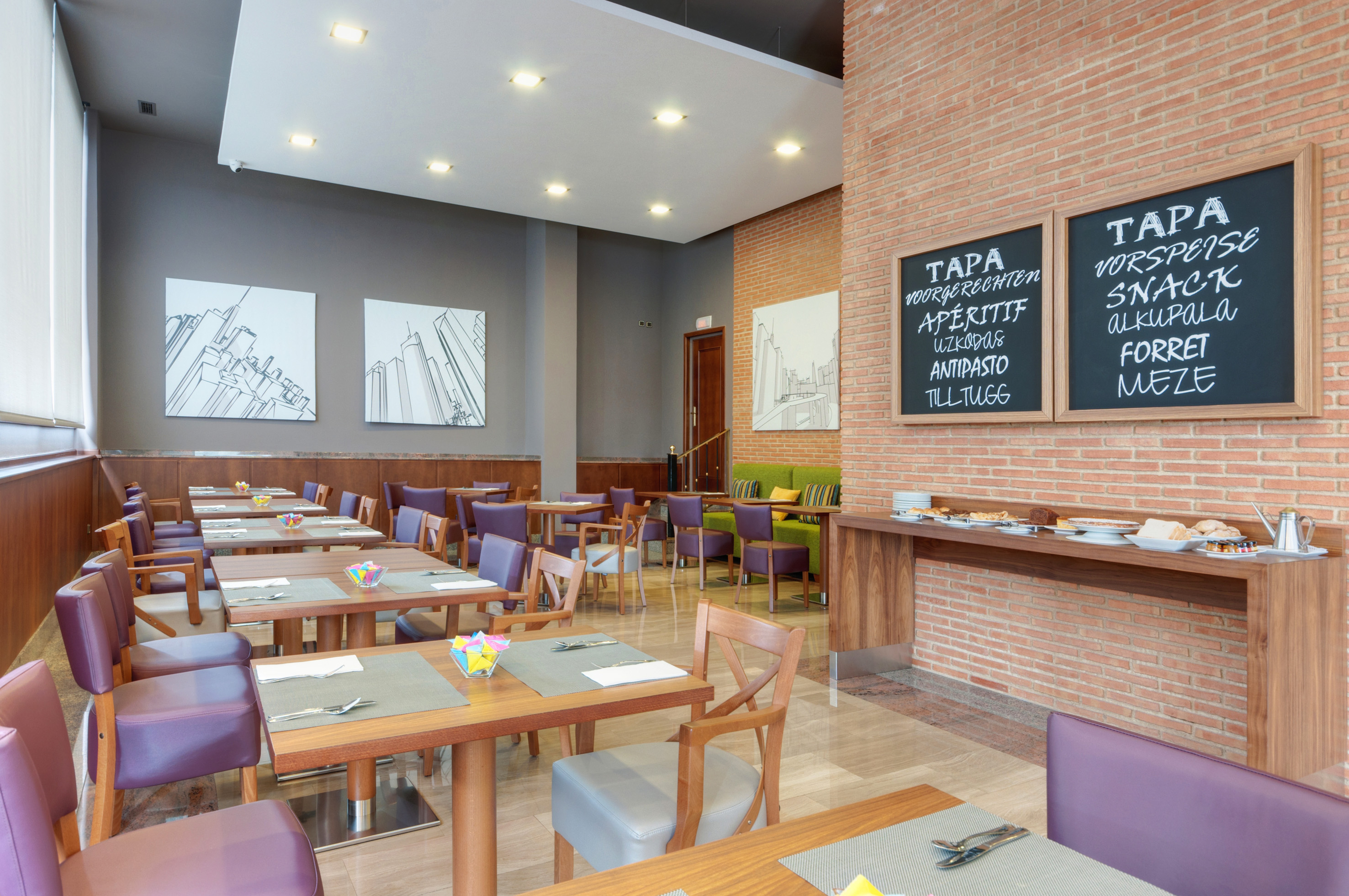 Modern hotel restaurant with buffet, tables, purple chairs, and brick wall.