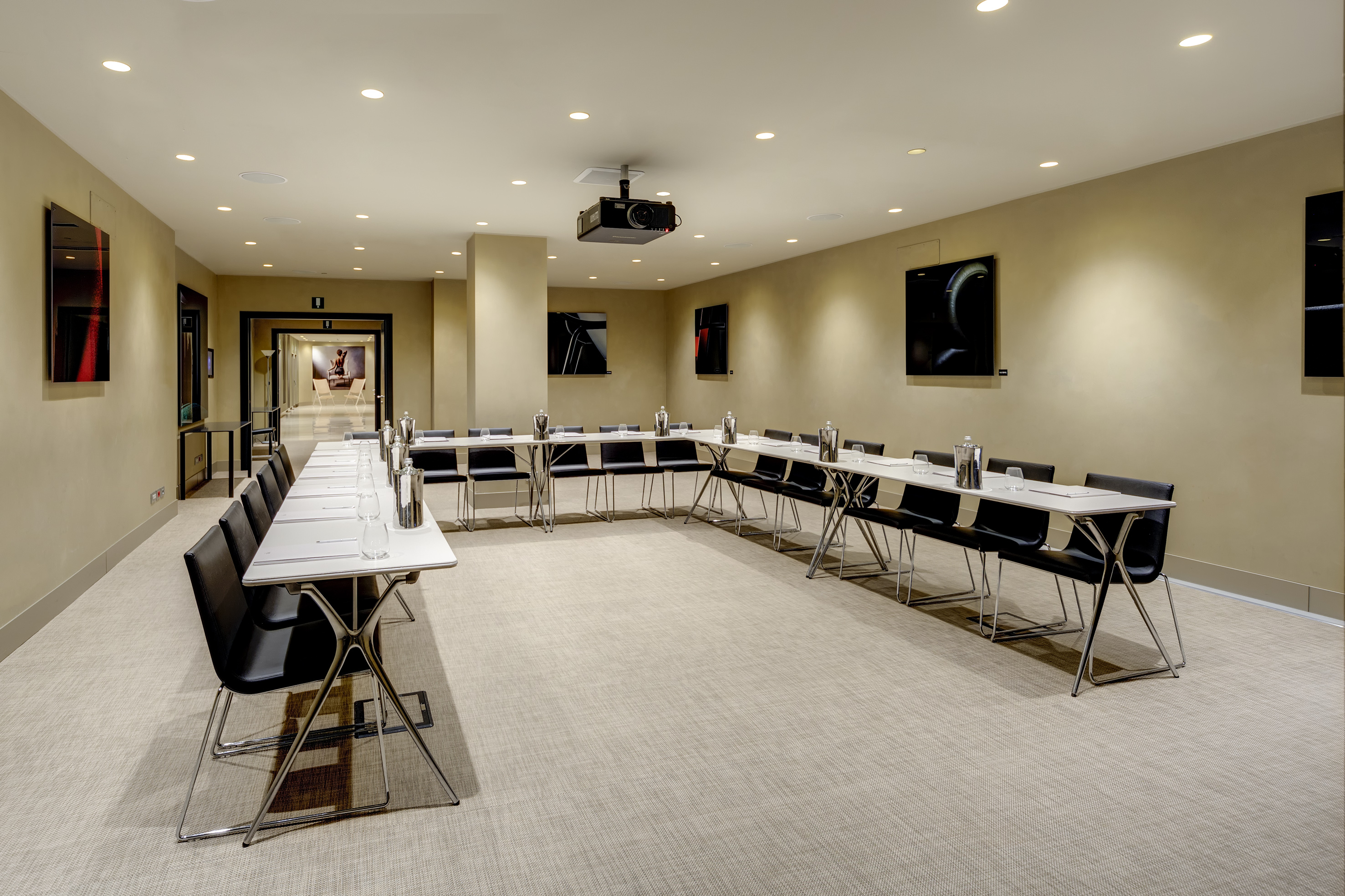 Modern conference room with U-shaped table, black chairs, and projector.