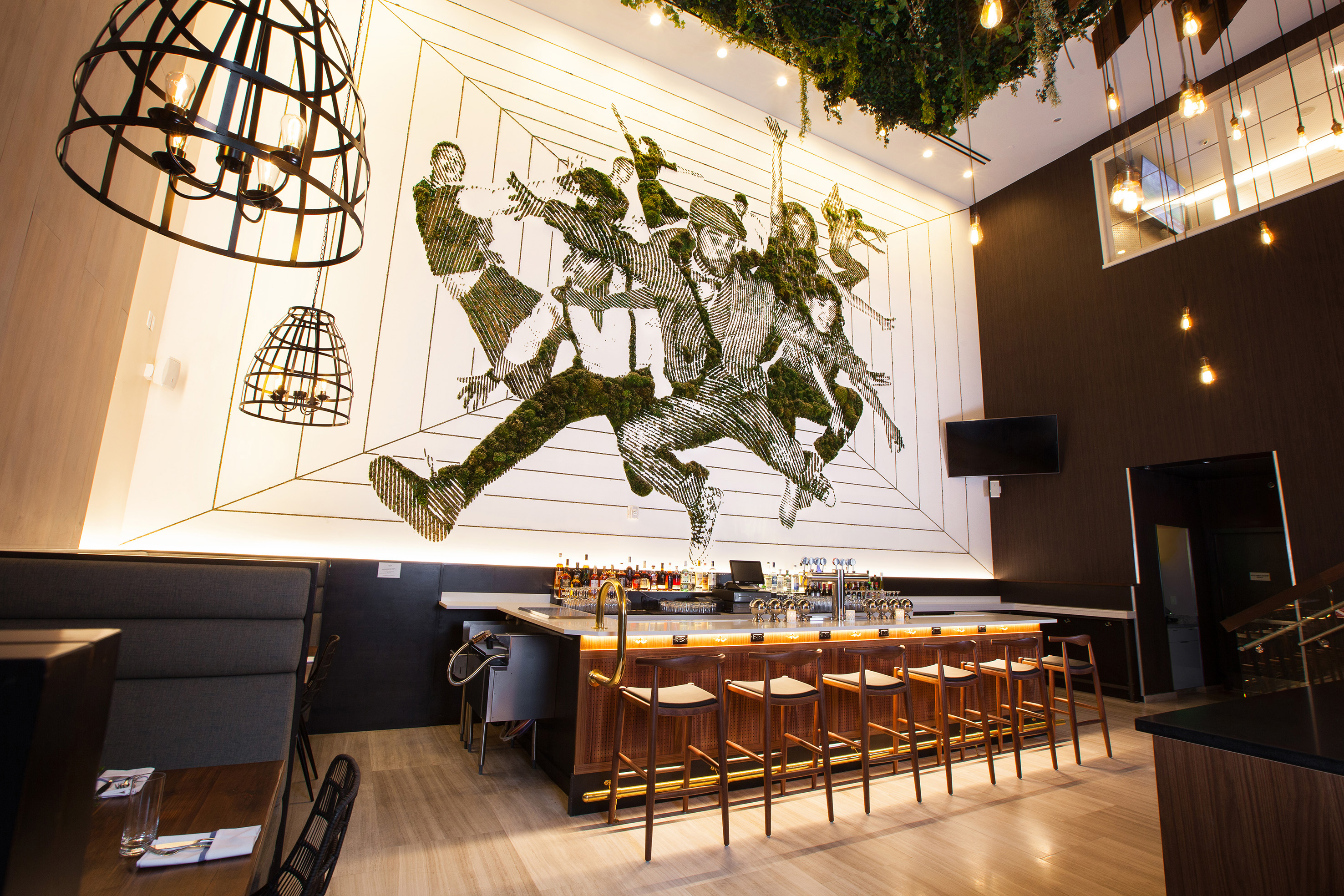 Modern bar interior with moss wall art, wooden stools, and geometric lighting.