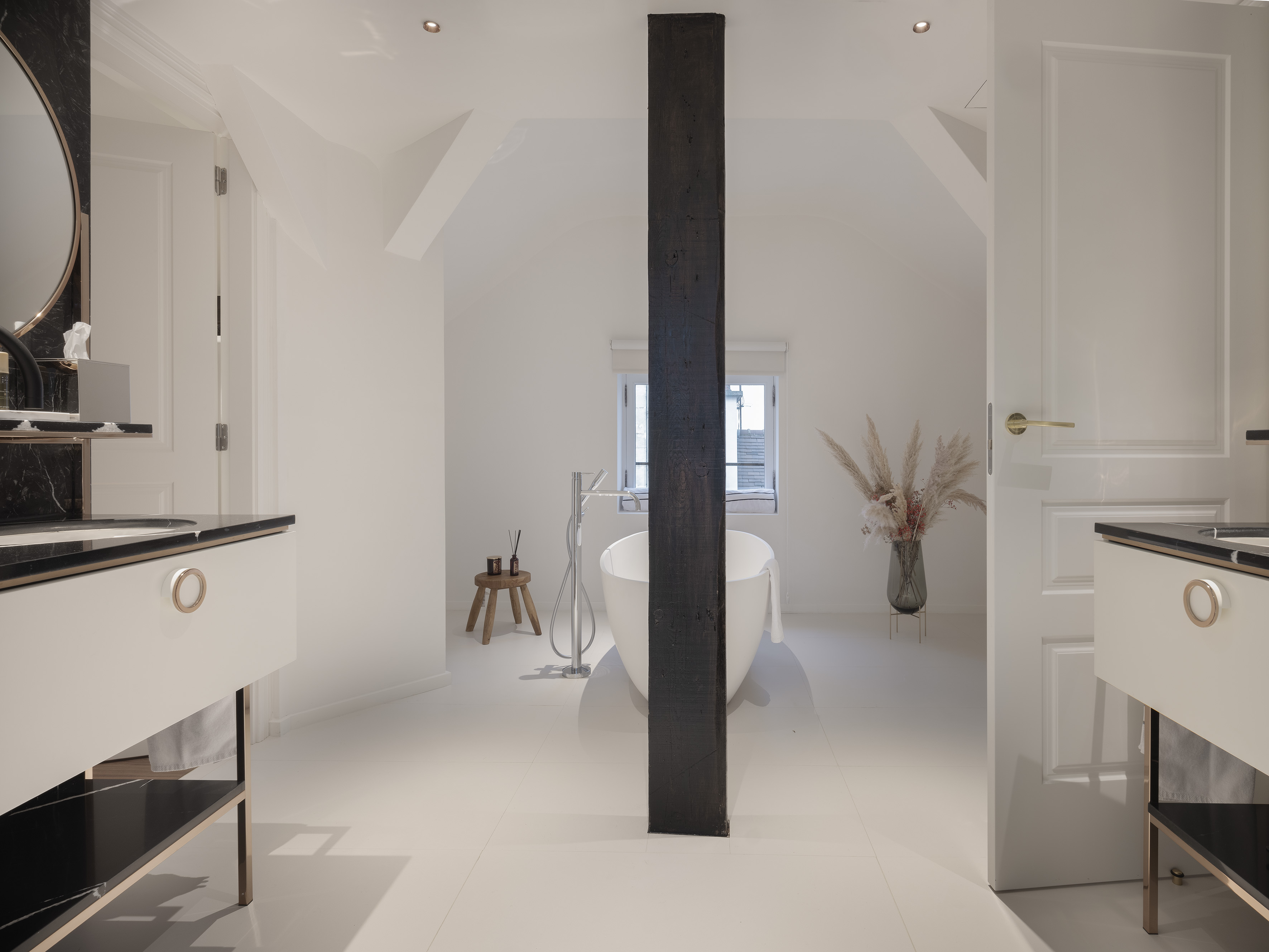 Modern luxury bathroom with freestanding tub, black marble vanities, dark beam.
