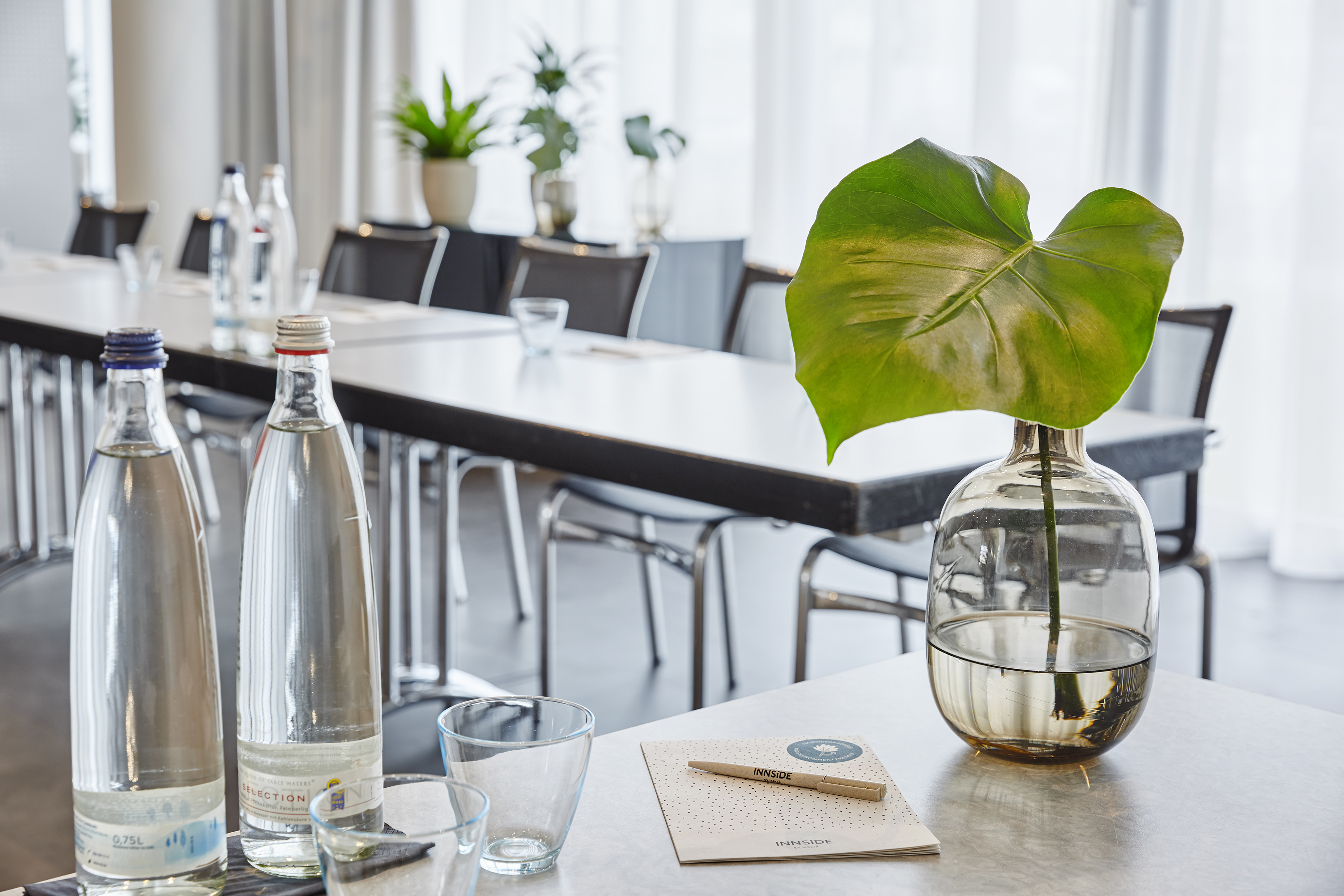 INNSIDE meeting room table with water bottles, notepads, and plant decoration.