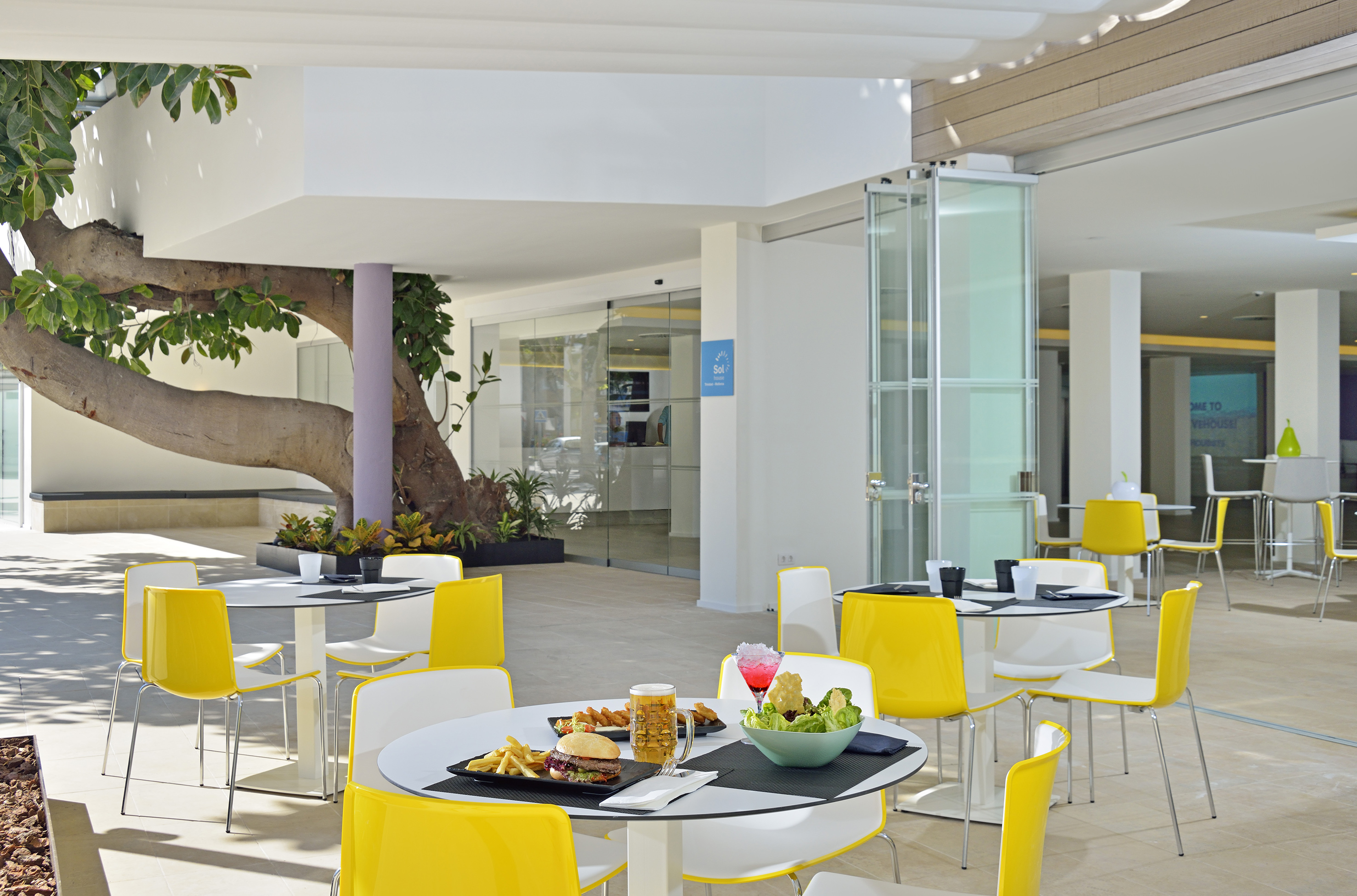 Outdoor cafe patio with yellow chairs, burgers, salads, and drinks.