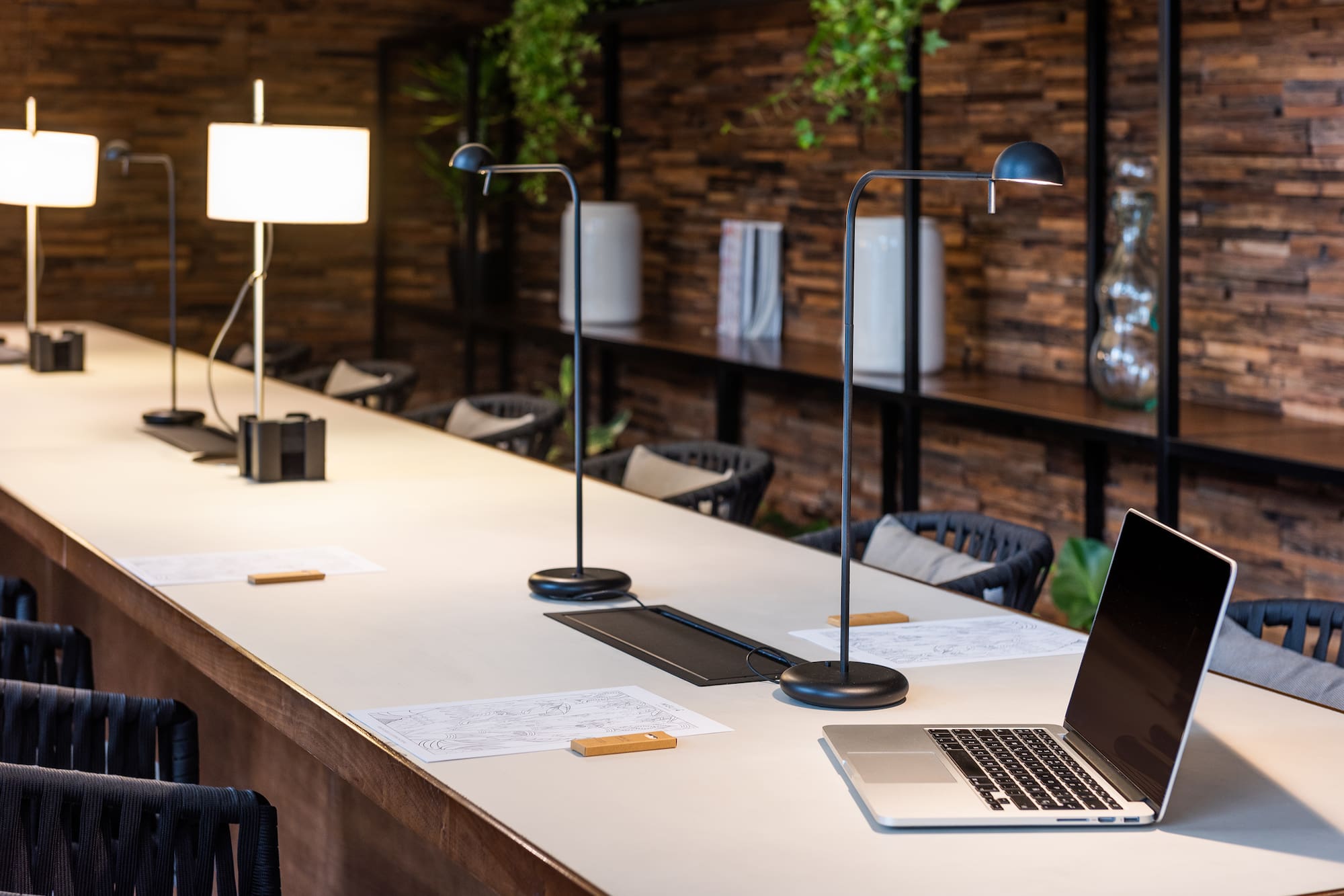 Contemporary co-working space with long desk, task lamps, and a laptop.