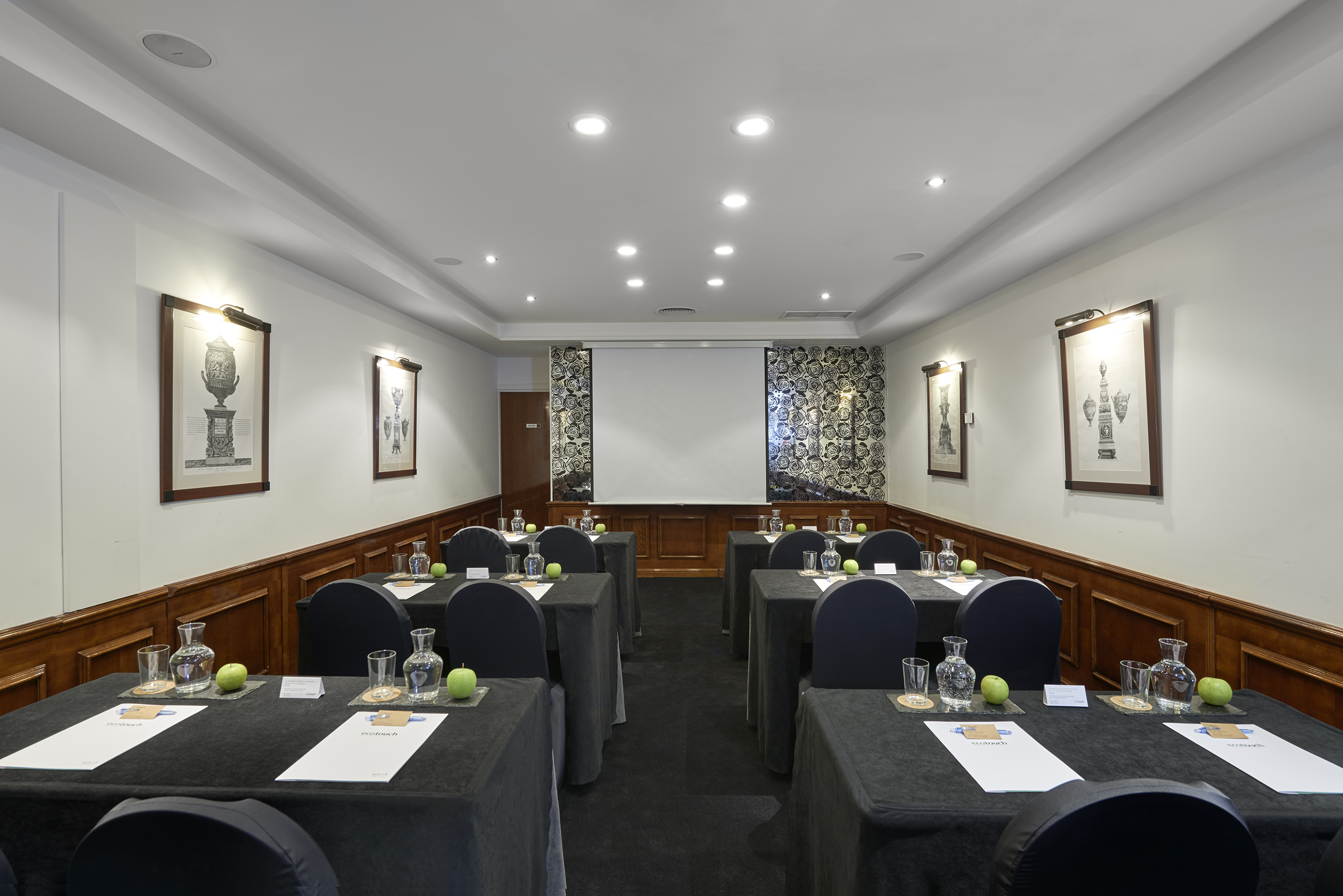 Professional conference room with tables, chairs, screen, and refreshments.