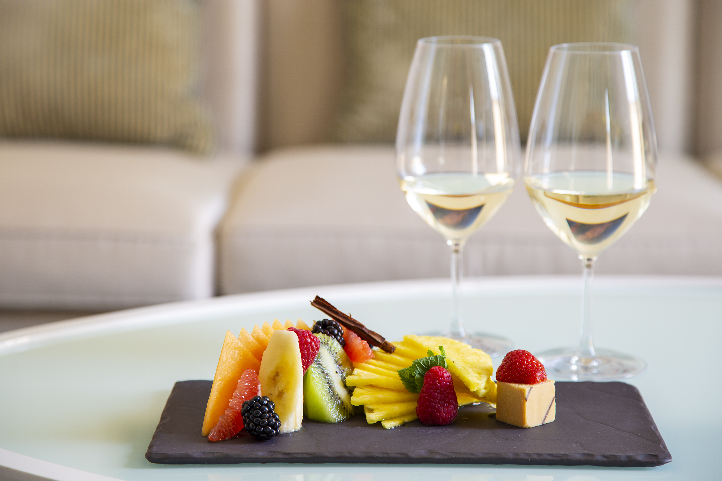 Gourmet fruit platter with white wine in a hotel suite living area.