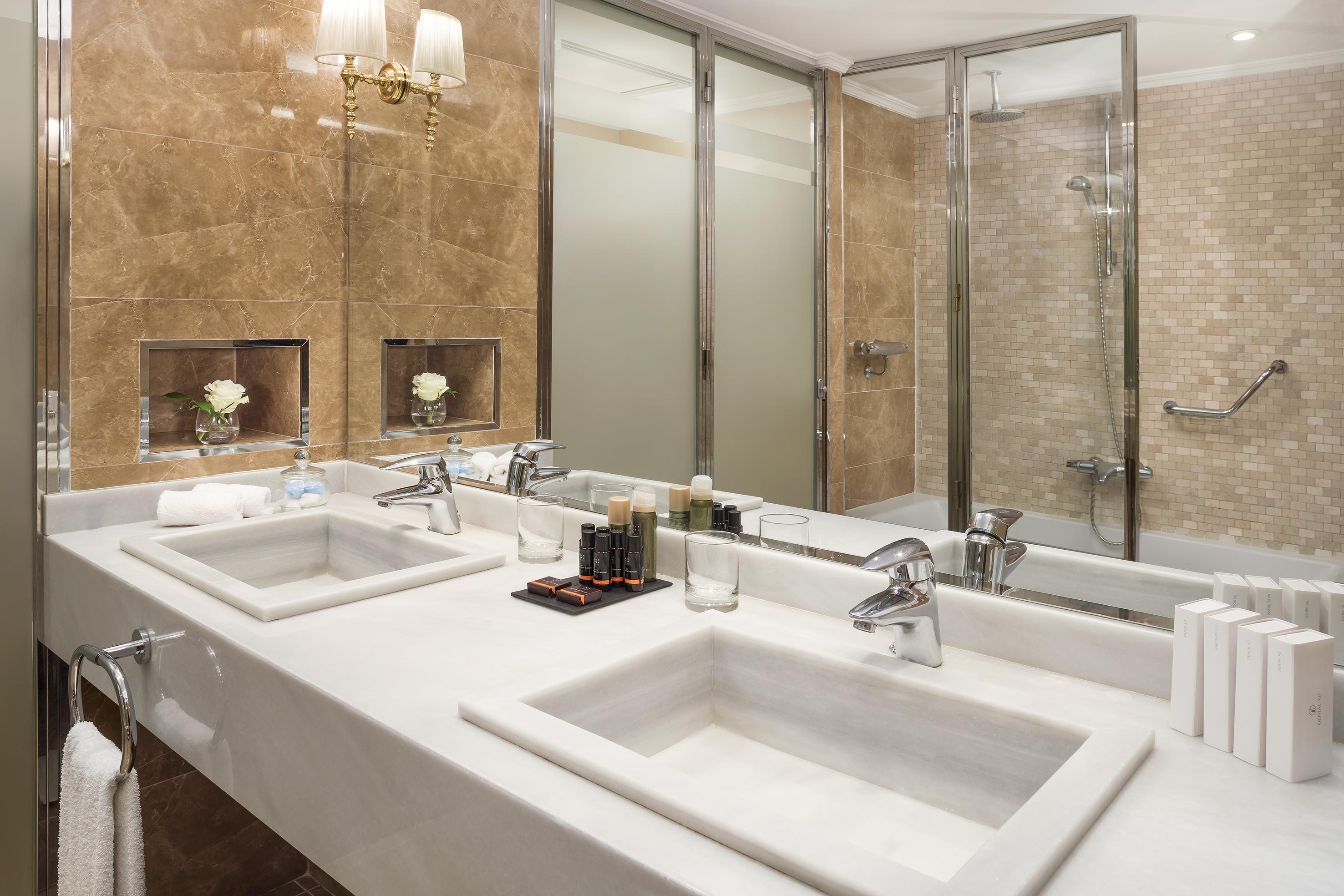 Elegant bathroom with dual marble vanity, modern glass shower, and brown tiled walls.