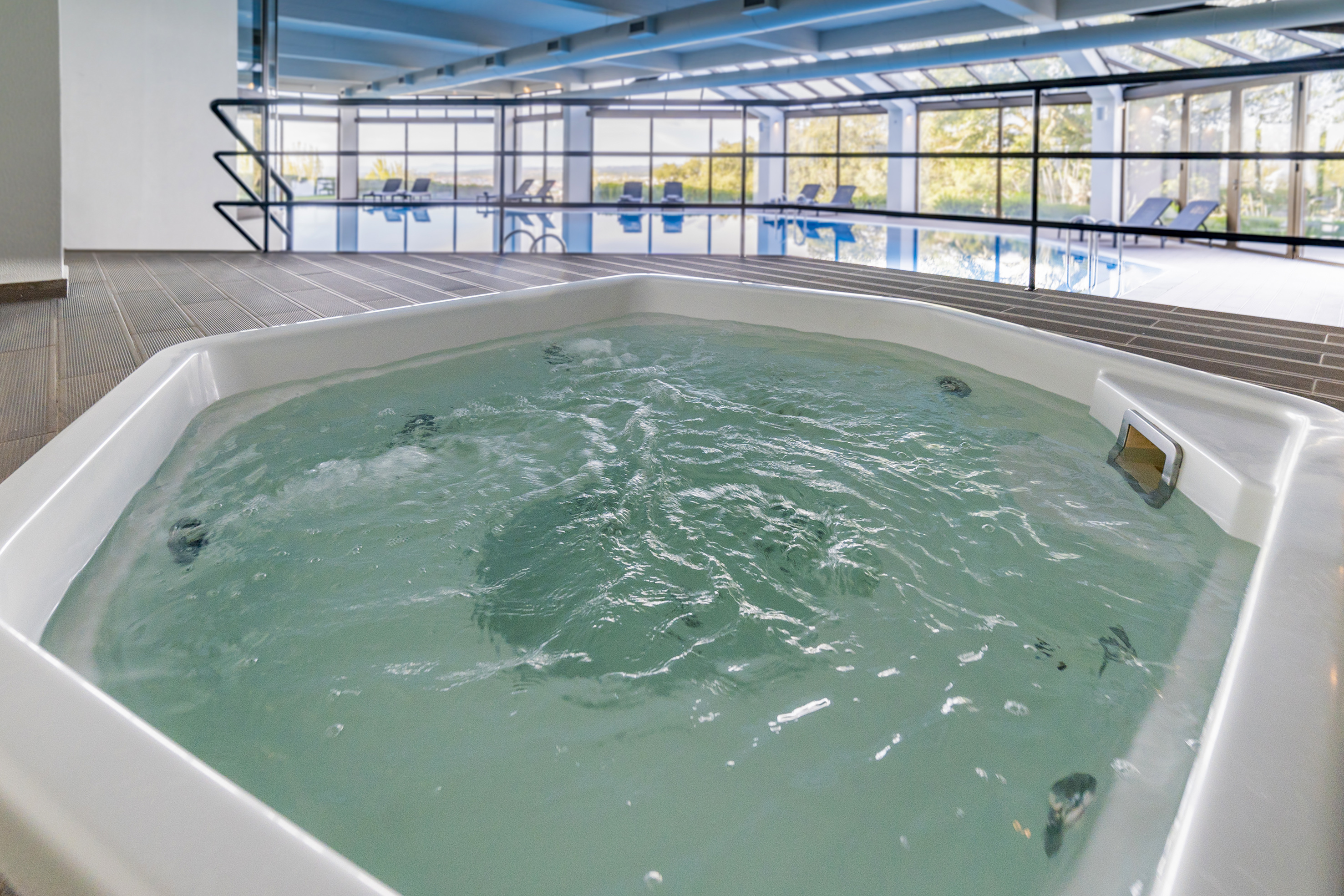 Bubbling hot tub in a bright indoor pool area with large windows.