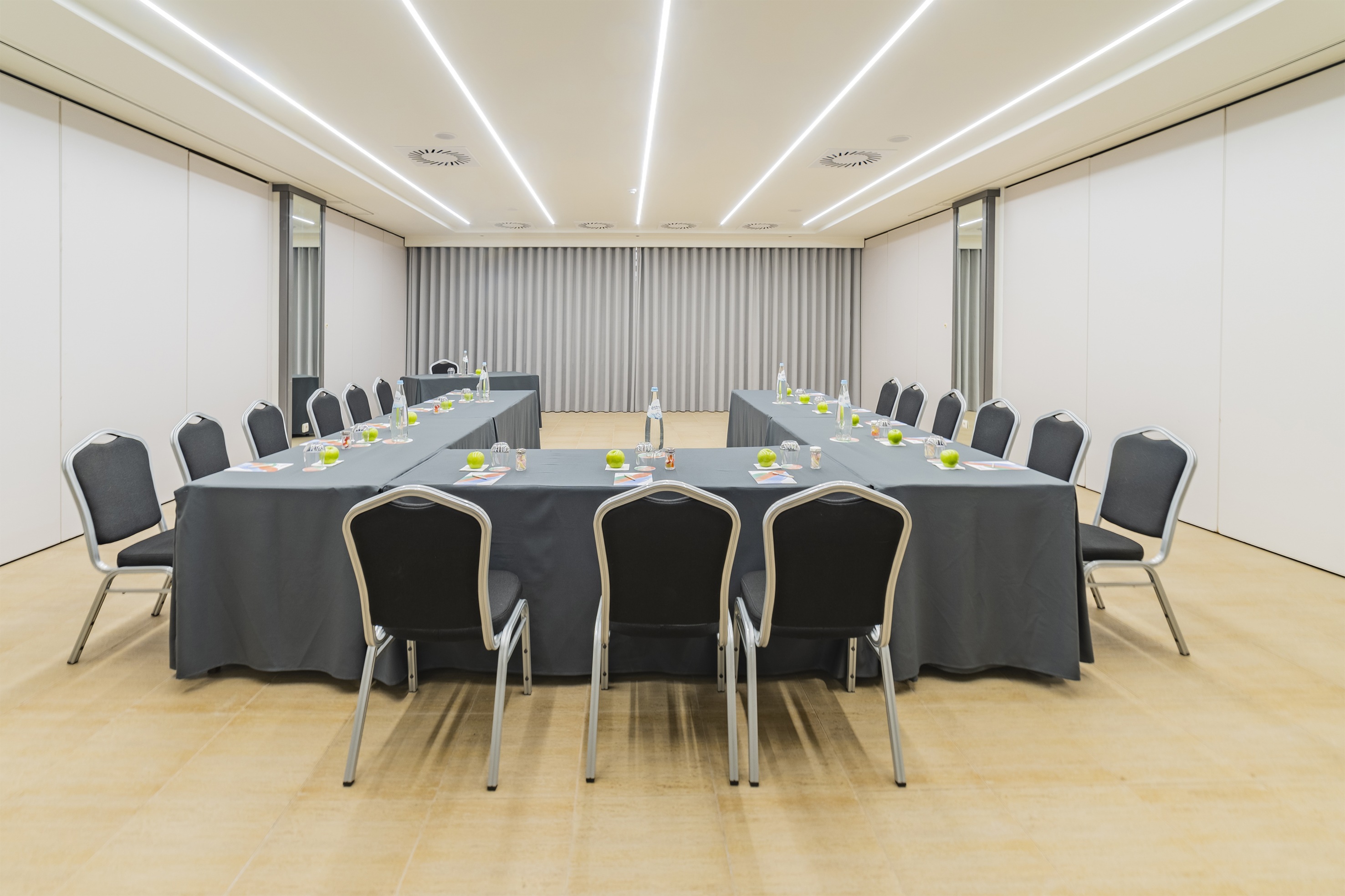 Modern U-shape conference room setup with grey tables, chairs, water bottles.