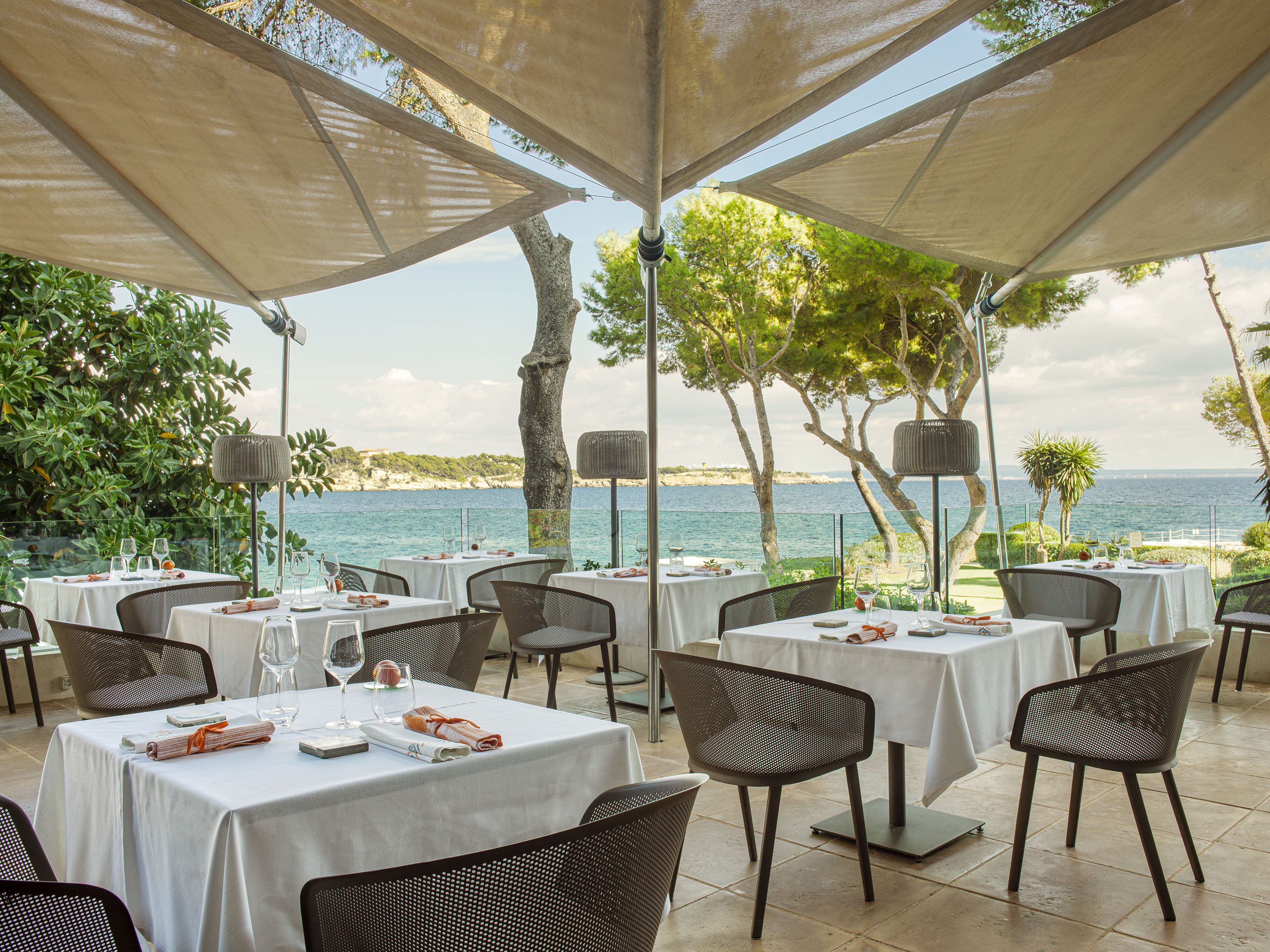 Outdoor restaurant patio with sea view under large umbrellas.