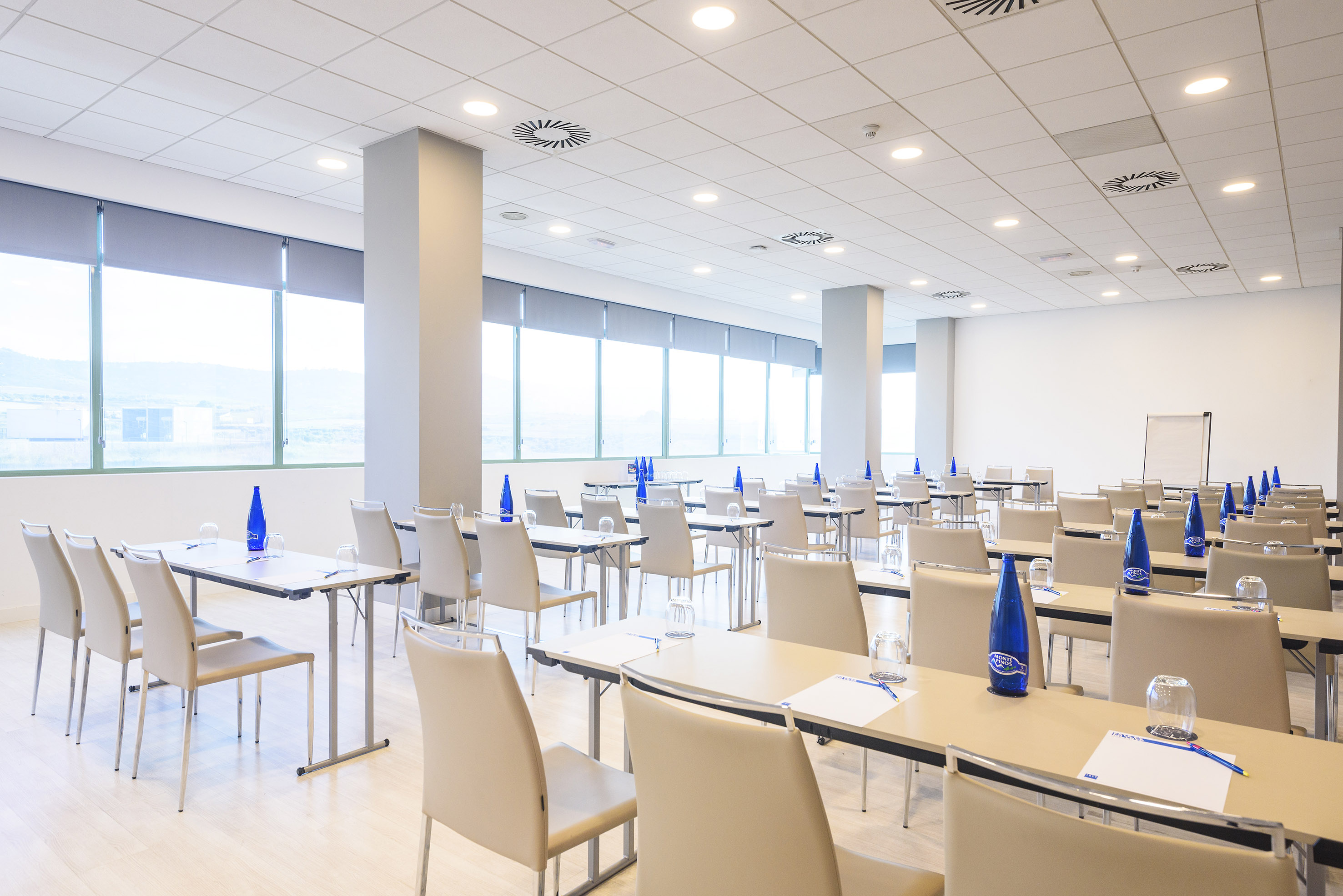Modern conference room with tables, chairs, large windows, and blue bottled water.