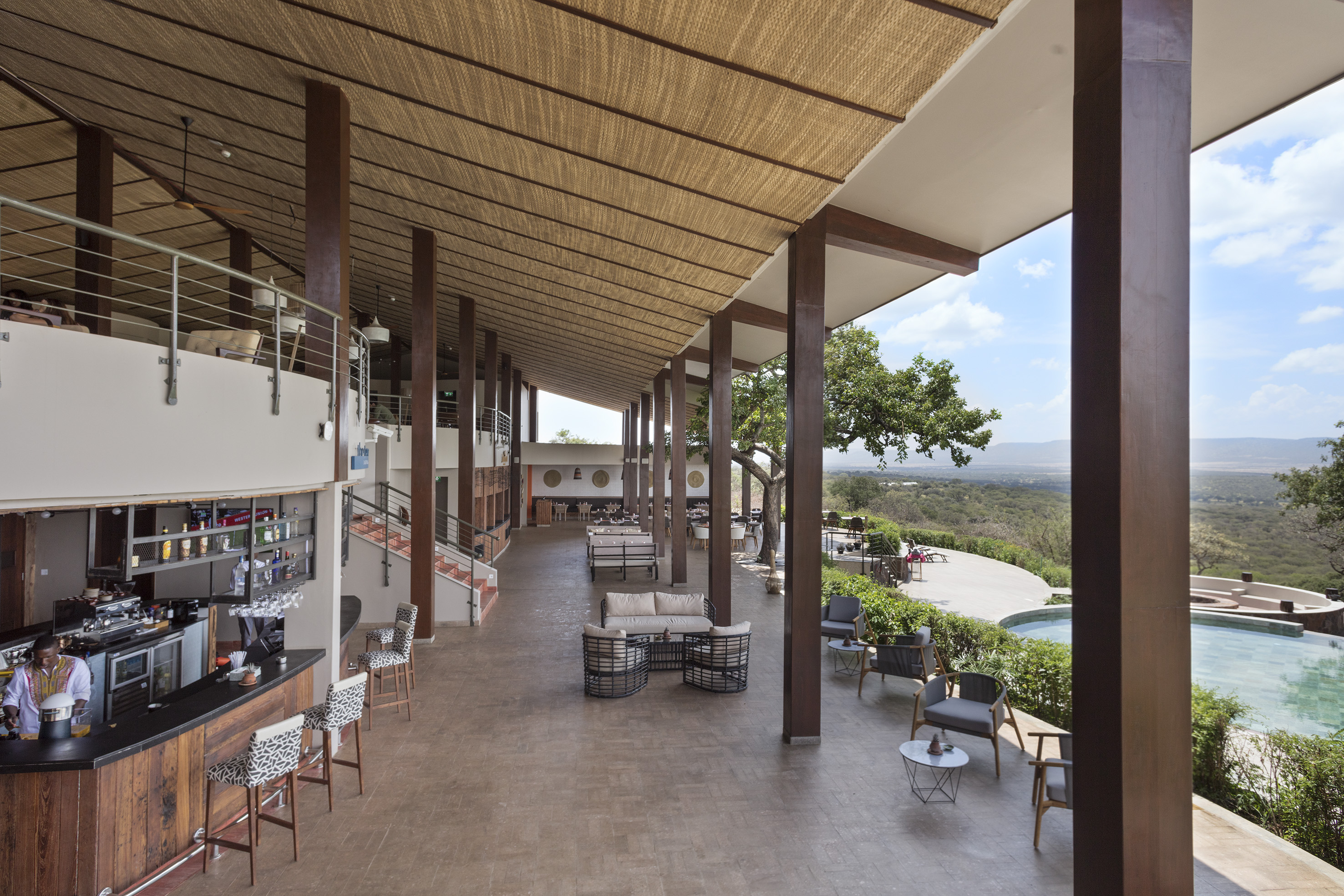 Safari lodge open-air lounge bar, woven ceiling, outdoor patio, and valley view.