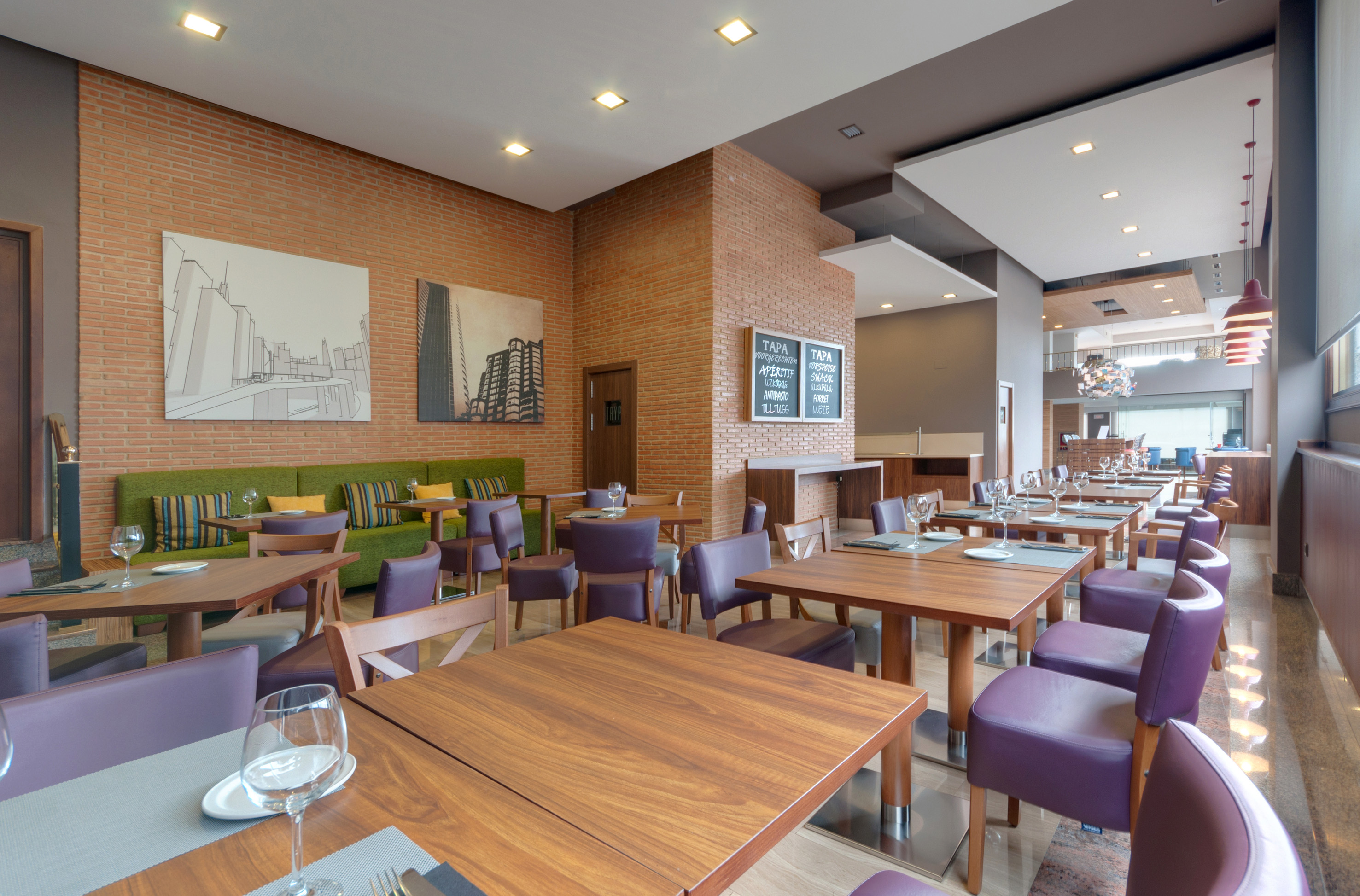 Modern restaurant interior with wooden tables, purple chairs, and brick walls.