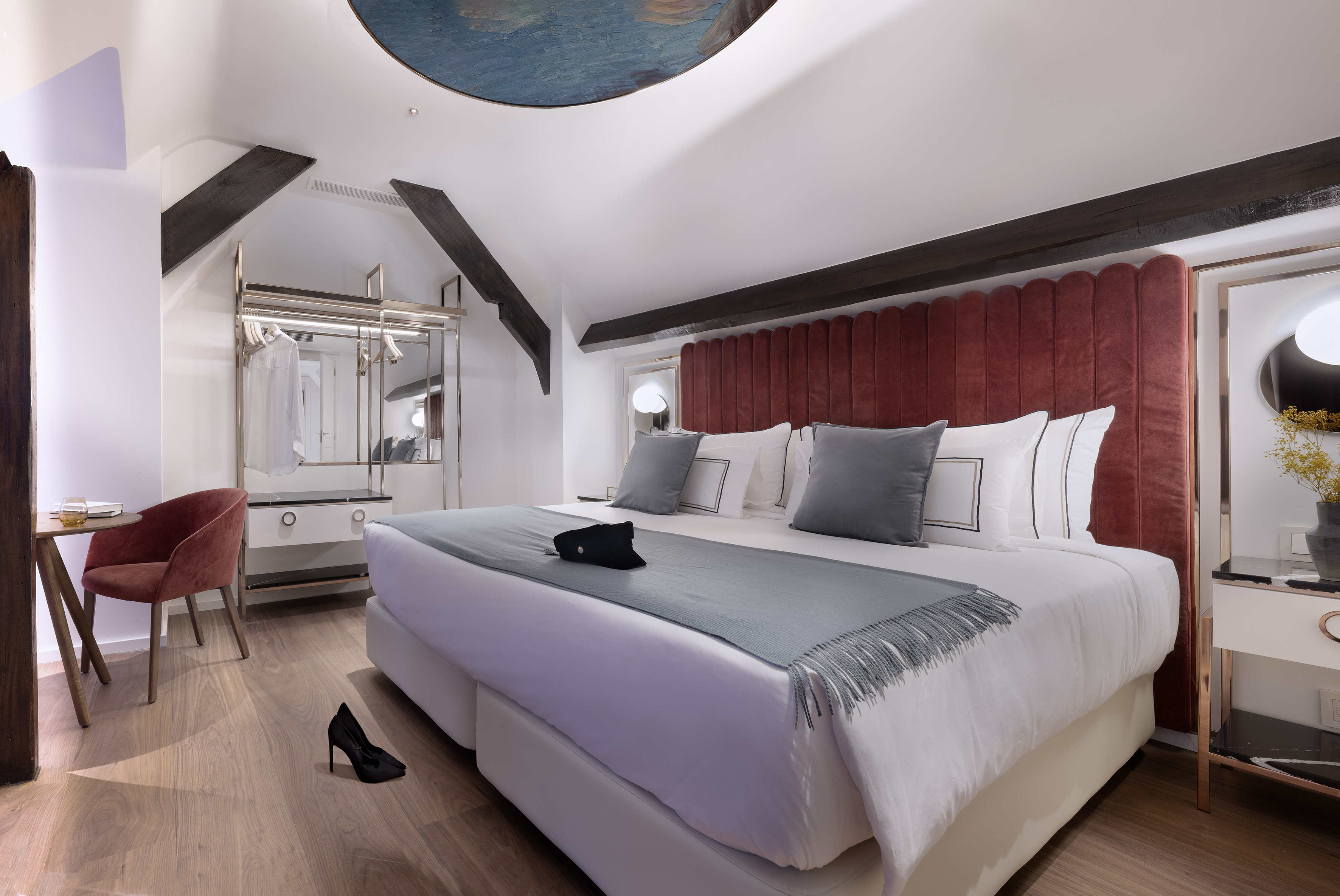 Modern hotel bedroom with king bed, red headboard, sloped ceiling, and wood beams.