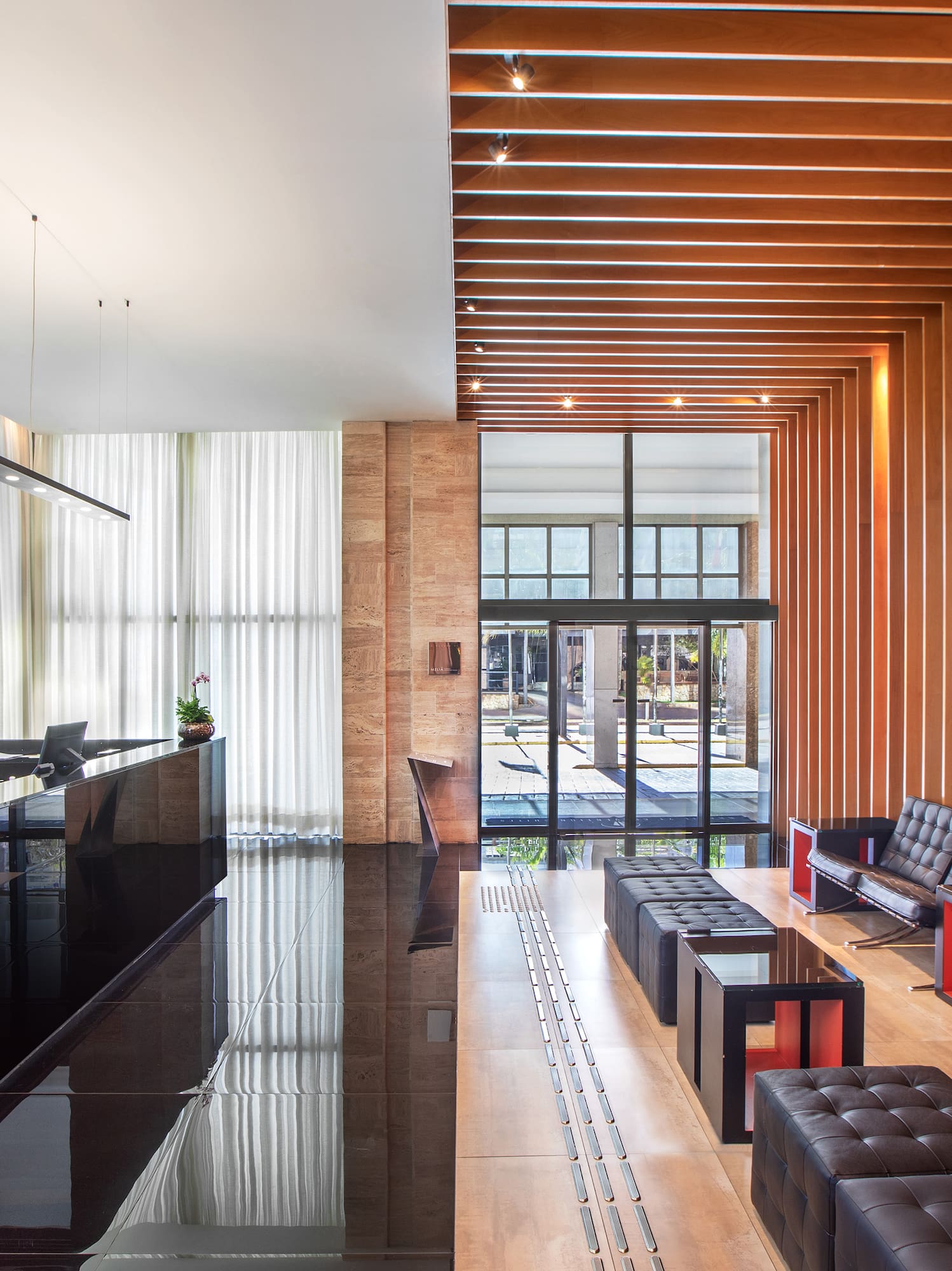 Modern hotel lobby with glossy black reception desk, wood slats, and leather seating.