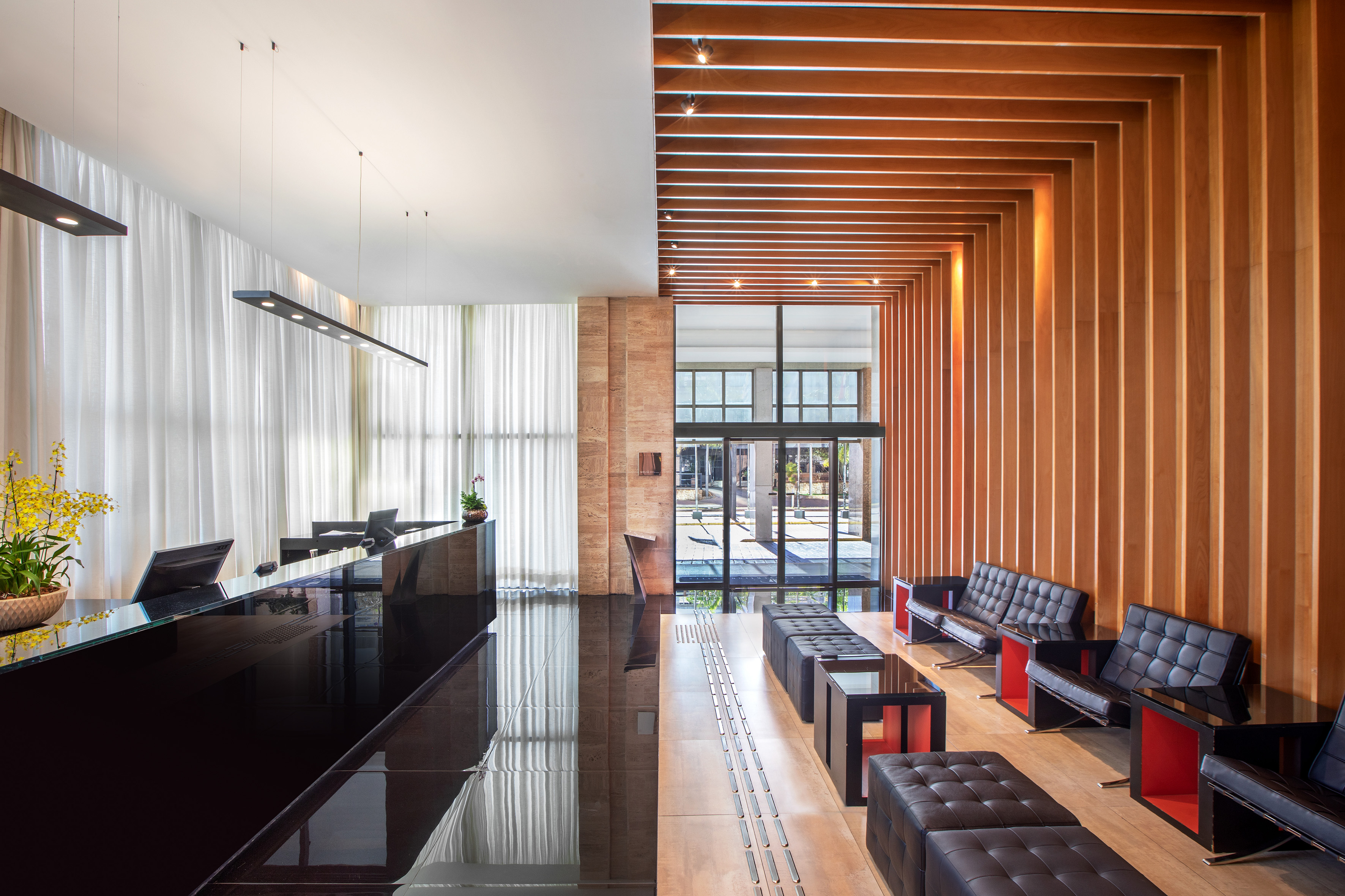 Modern hotel lobby with glossy black reception desk, wood slats, and leather seating.