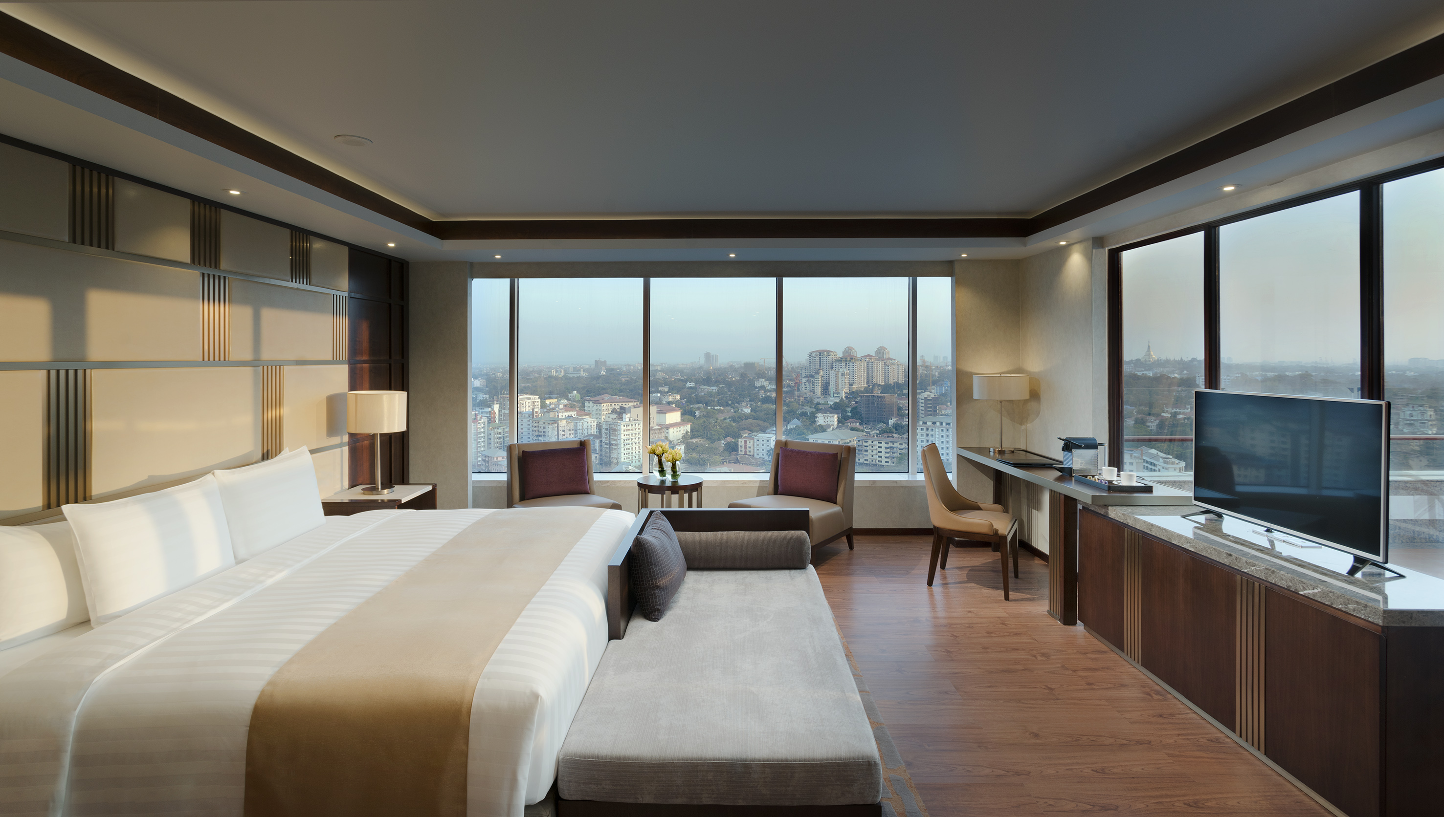 Modern luxury hotel room with panoramic city view and king bed.