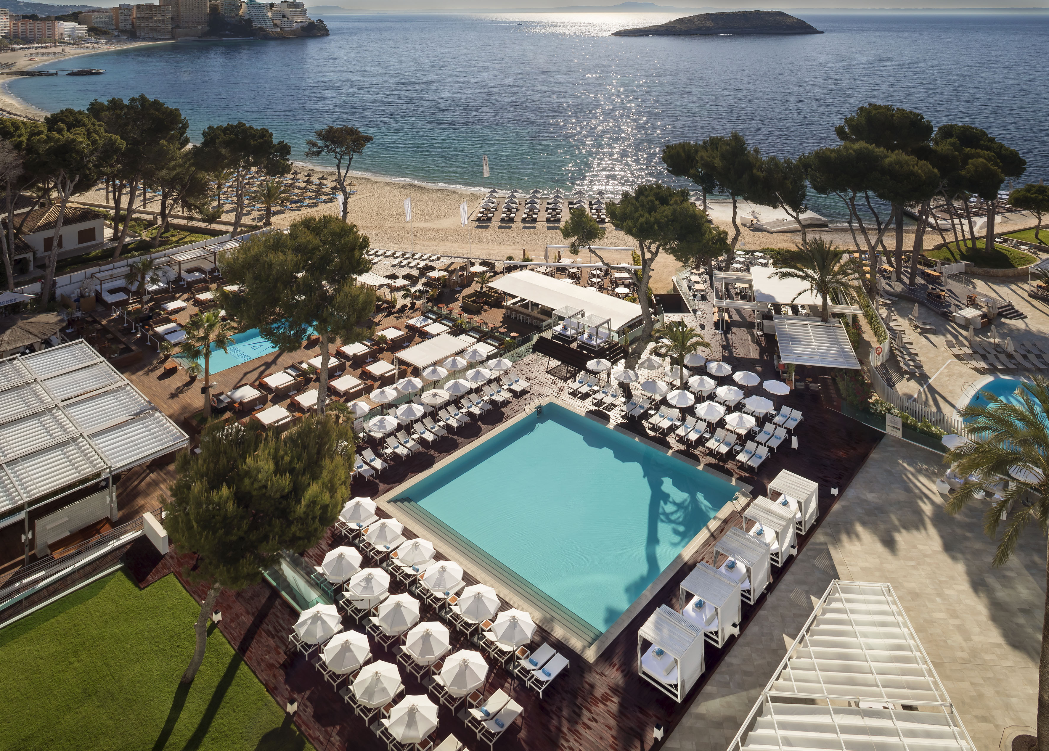Luxury beach resort aerial: pool, umbrellas, cabanas, sandy beach, sparkling ocean.