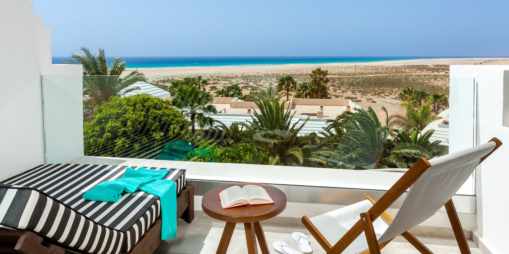 a deck with chairs and a table on a balcony overlooking a beach